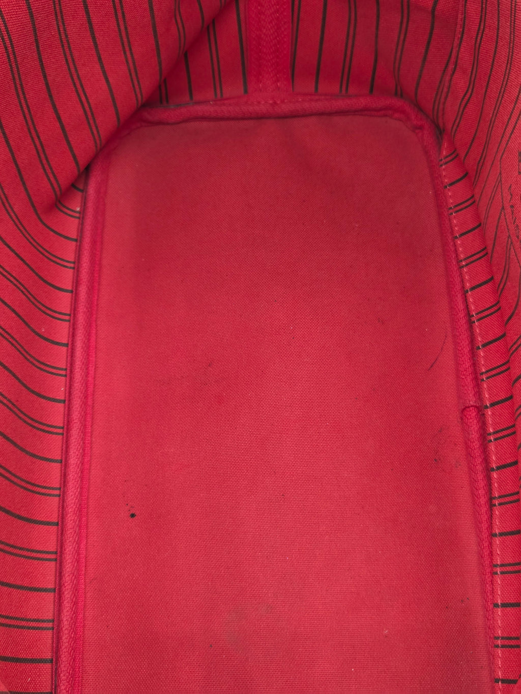 Close-up of a red fabric interior with a smooth central panel and striped red-and-black fabric lining along the edges.