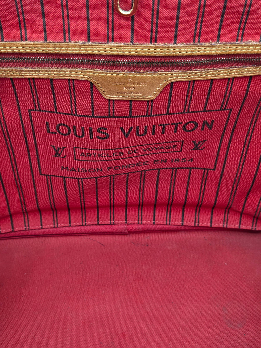 Close-up of a Louis Vuitton red and black pinstriped fabric bag interior, showing the brand label and zipper trim.