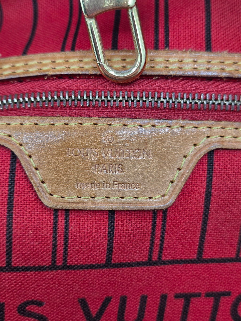 Close-up of a Louis Vuitton bag featuring a red canvas body with black stripes, tan leather zipper trim, and a metal D-ring closure. The embossed leather patch reads 'LOUIS VUITTON PARIS made in France'.