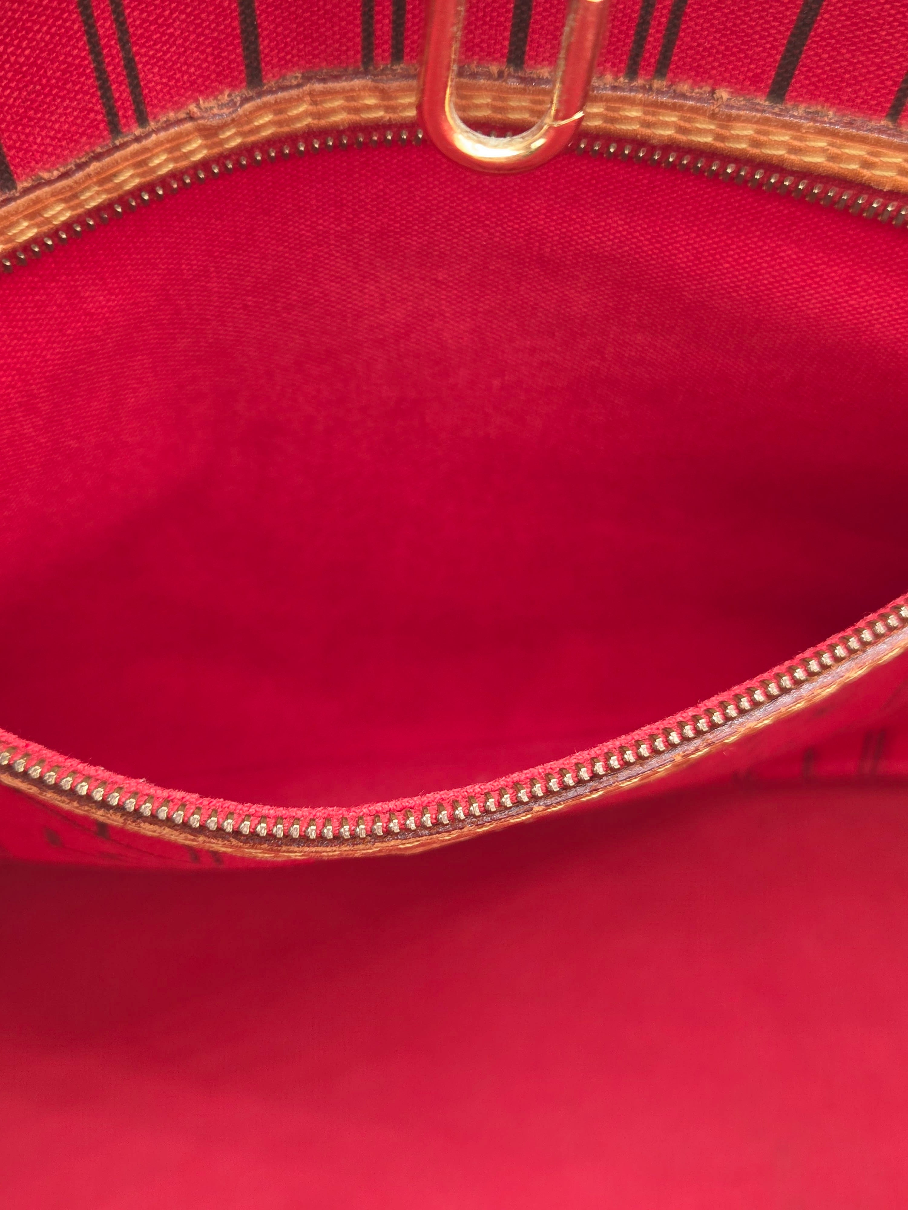 Close-up of a bright red fabric pouch or clutch showing the interior lining, a gold-tone zipper, and part of a gold metal pull.