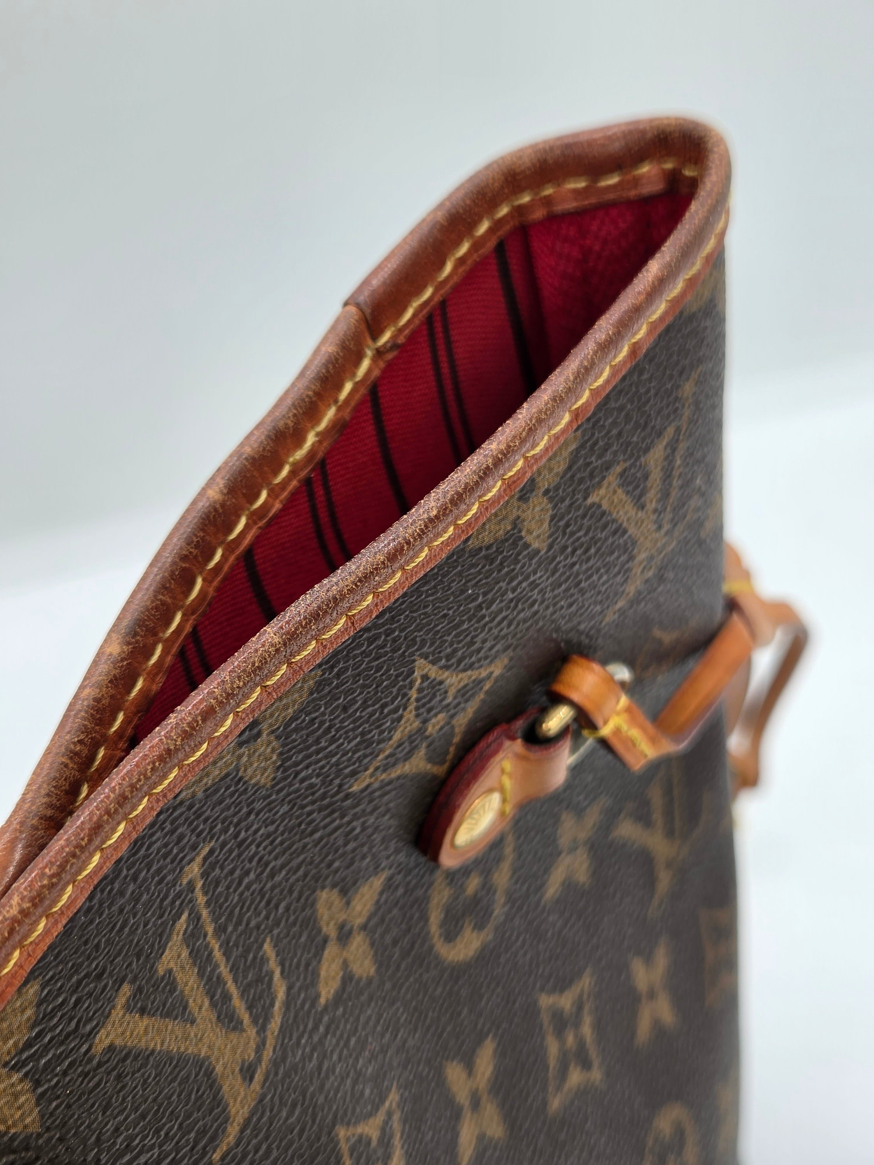 Close-up of a Louis Vuitton monogram canvas bag with brown leather trim and a red striped interior lining.
