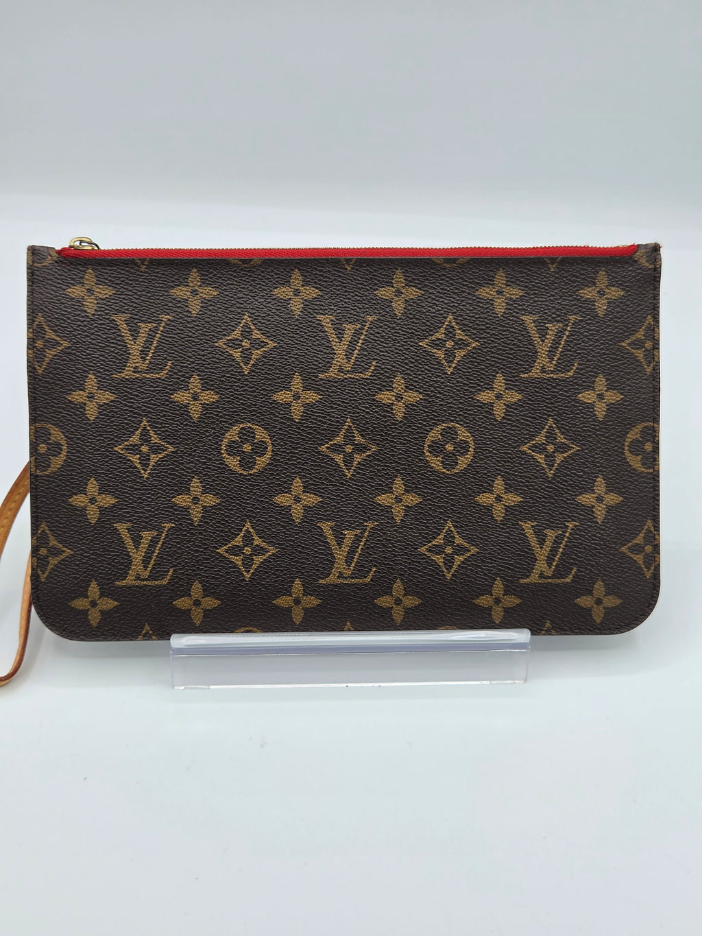 A Louis Vuitton monogram canvas pouch with a red zipper trim, displayed on a clear acrylic stand against a light gray background.