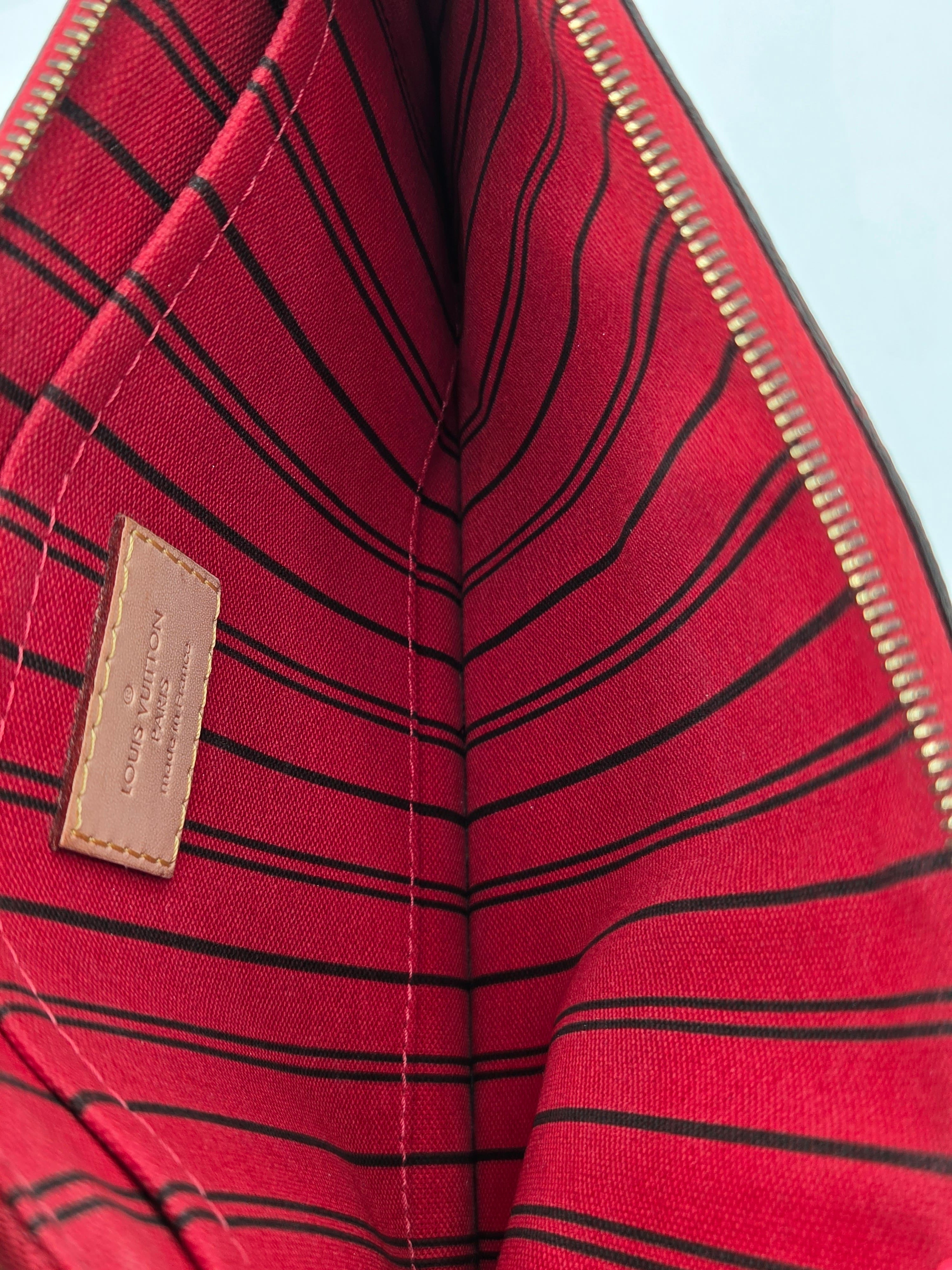 Close-up of the interior lining of a Louis Vuitton bag, featuring a vibrant red fabric with thin black stripes and a tan leather brand label.