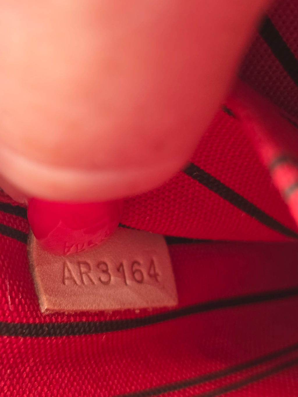 Close-up of a red woven textile with black stripes and a small beige size tag stamped with the number AR3164.