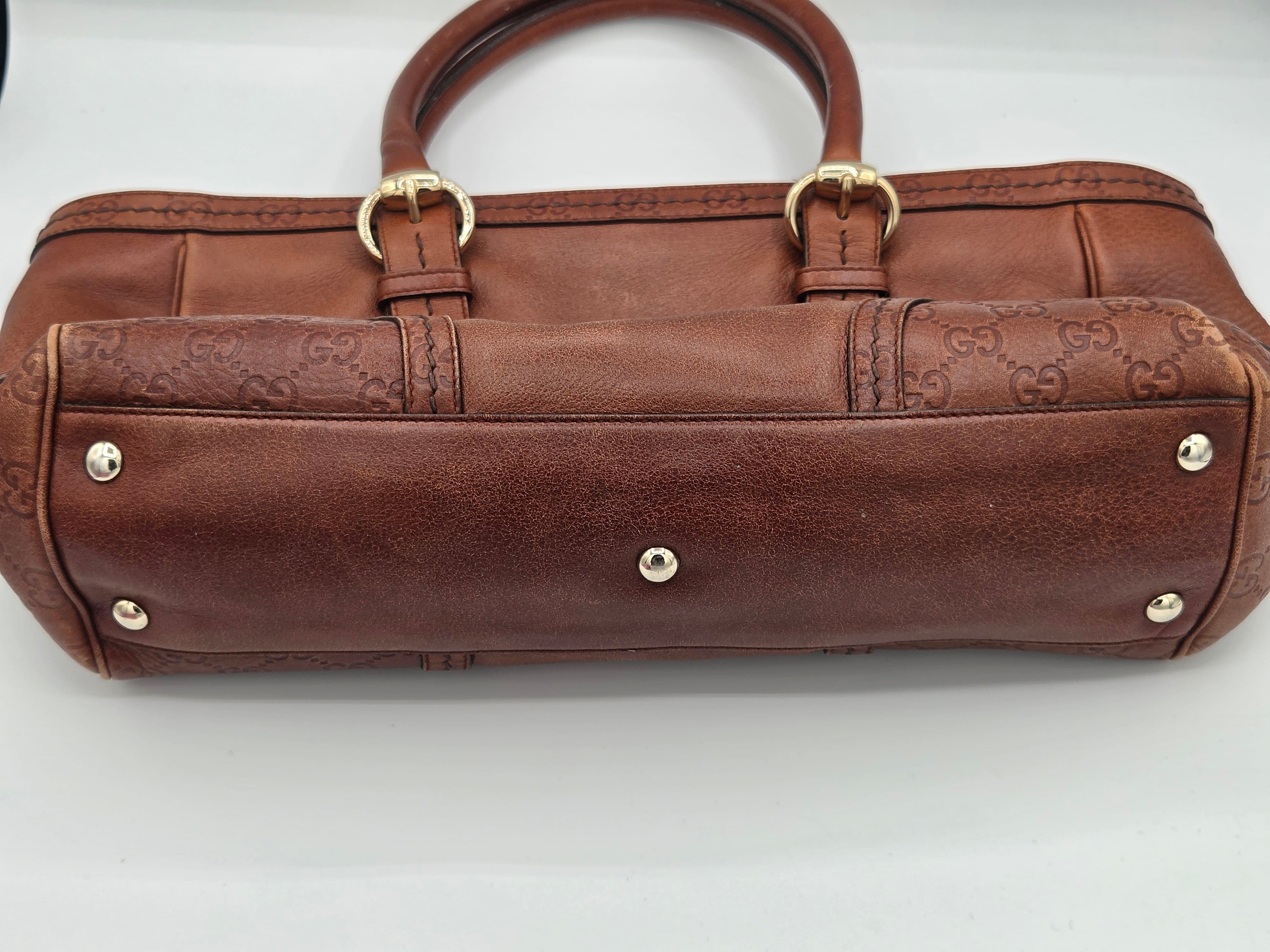 A brown leather handbag with embossed monogram pattern, gold-tone hardware, and silver-tone studs, photographed on a plain light background.