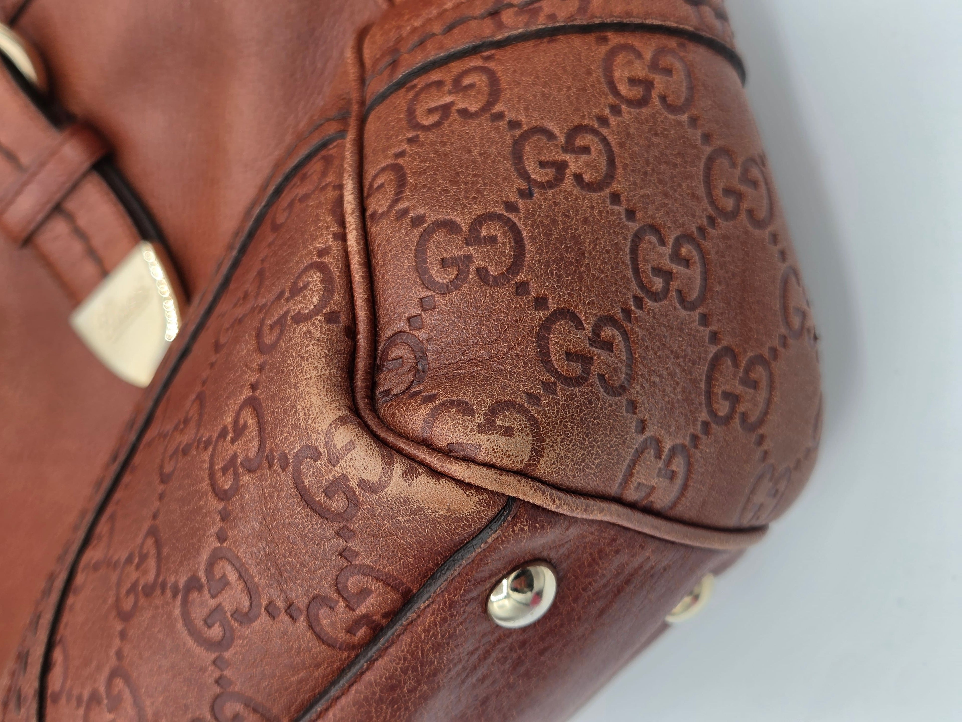 Close-up of a brown leather handbag featuring the embossed Gucci GG monogram pattern and gold-tone hardware.