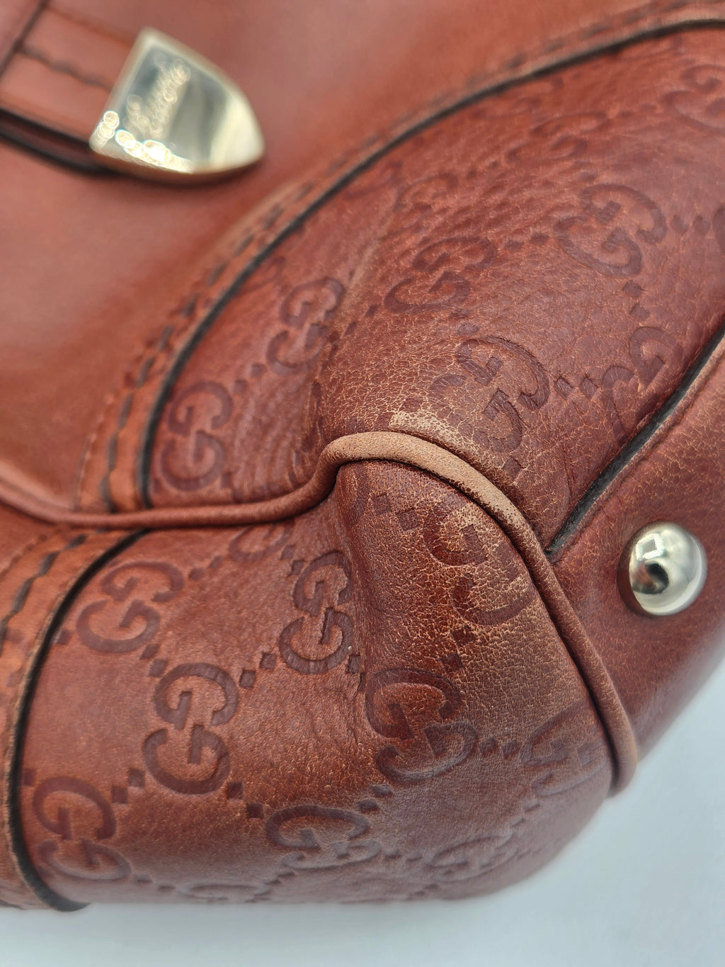 Close-up of a brown leather handbag featuring an embossed Gucci GG monogram pattern and gold-tone hardware.