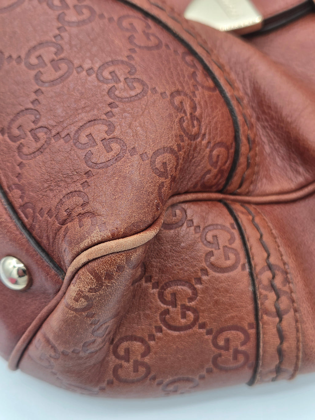 Close-up of a brown leather handbag featuring the embossed Gucci GG monogram pattern, with visible gold-tone hardware and black contrast stitching.