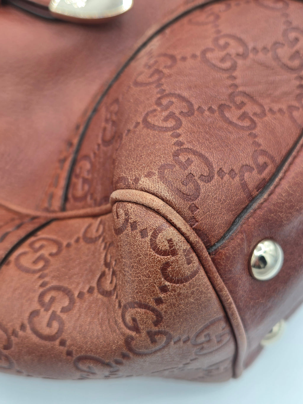 Close-up of a brown leather handbag featuring an embossed interlocking GG monogram pattern, with gold-tone metal studs and a curved black leather trim.