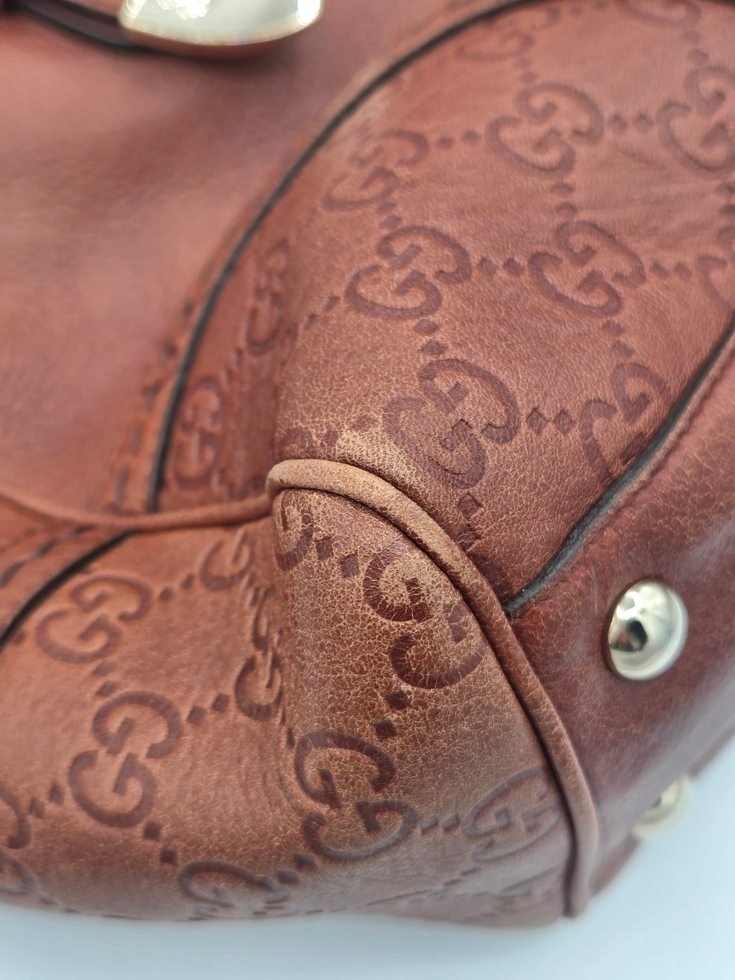 Close-up of a brown leather handbag featuring an embossed interlocking GG monogram pattern, with gold-tone metal studs and a curved black leather trim.