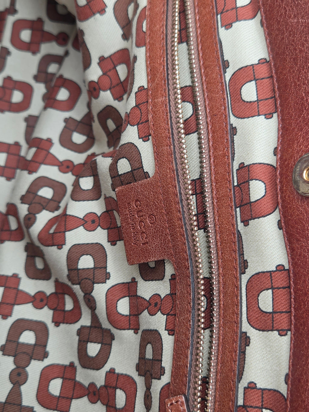 Close-up of a leather zippered pocket on a jacket, featuring a brown leather tab with the Dri-Dri logo and a patterned lining with brown horsebit motifs on a light background.