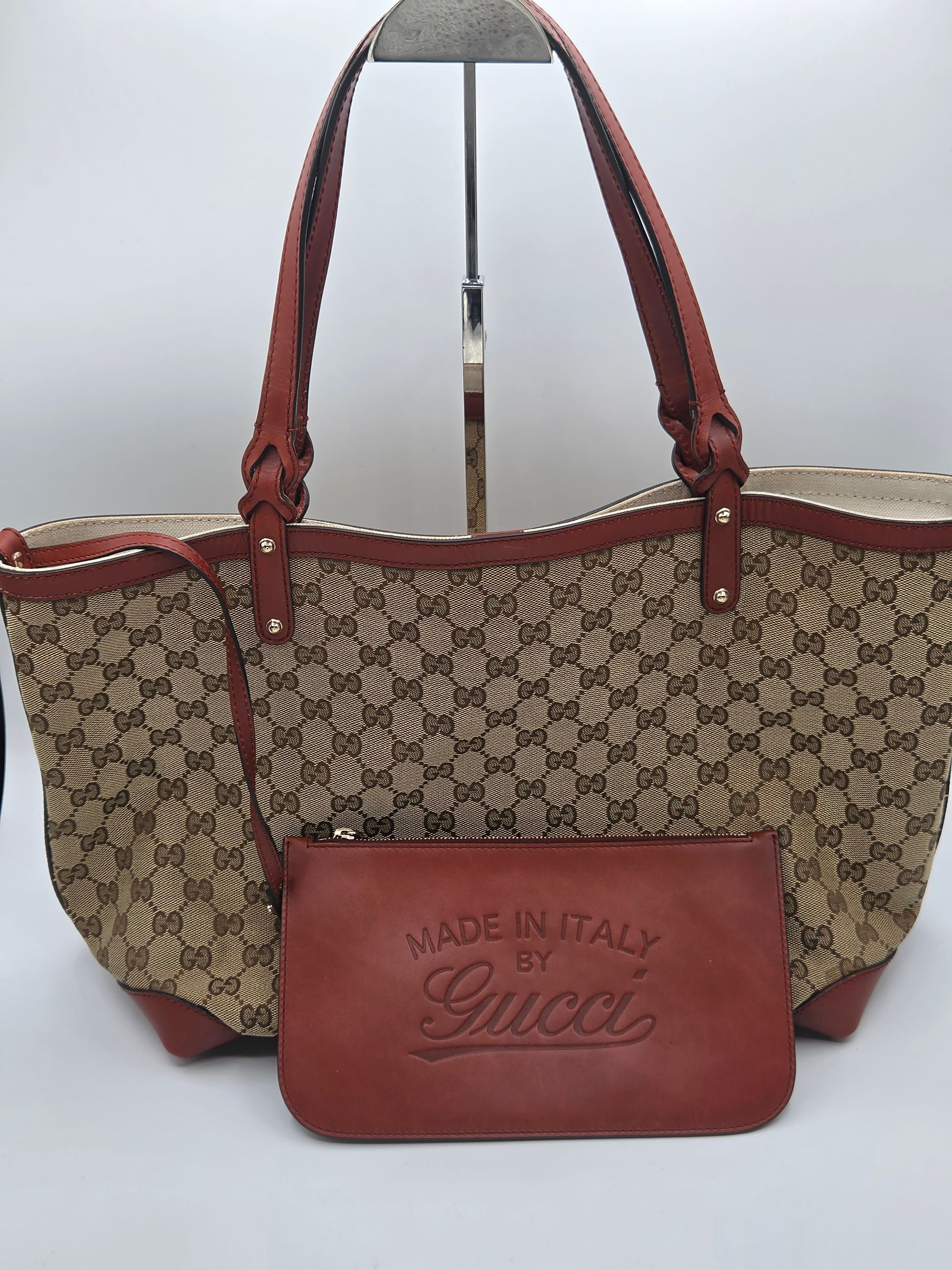 Gucci monogram canvas tote bag with brown leather handles and trim, shown with a matching brown leather pouch in front on a white studio background.