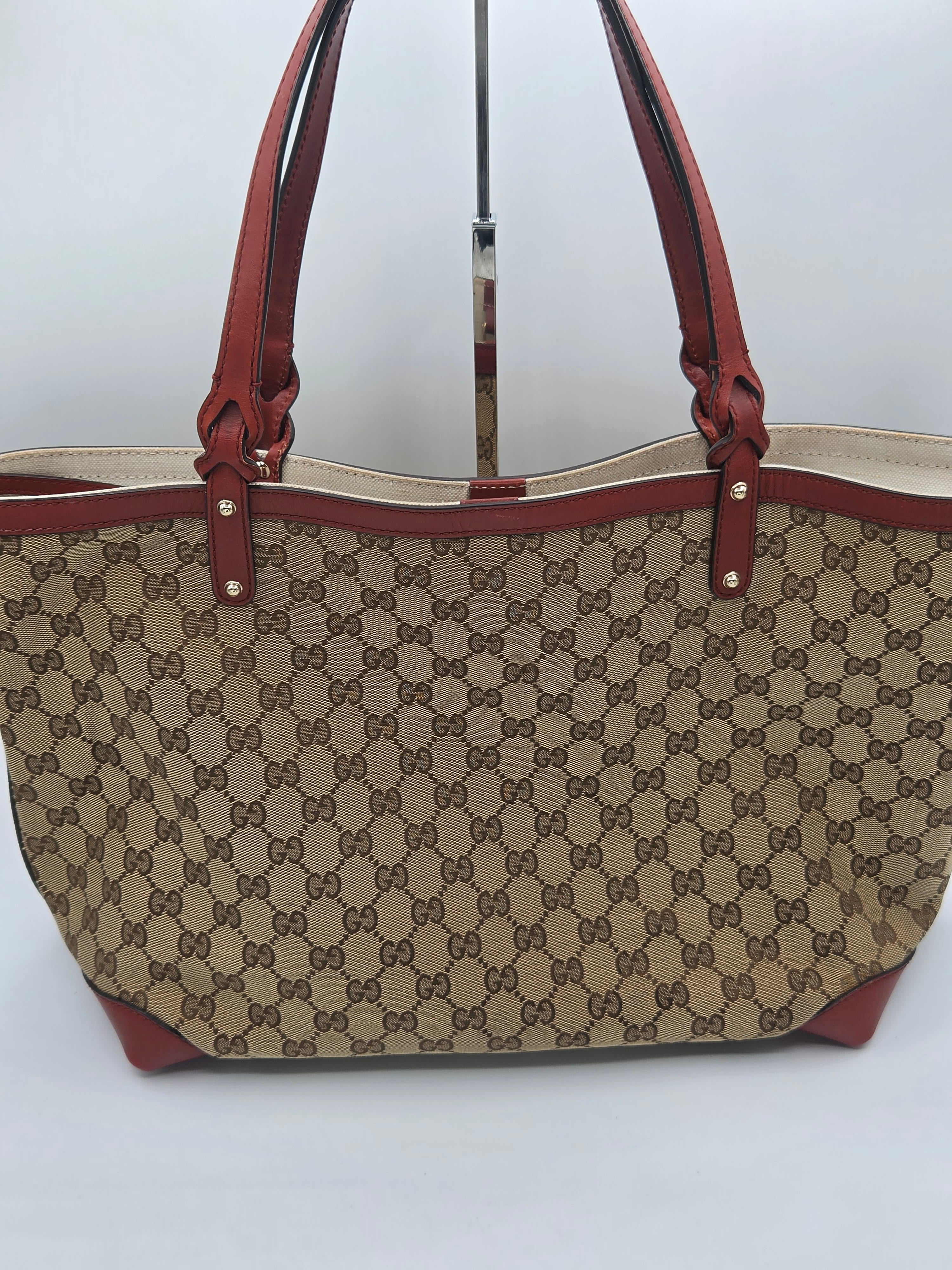 A vintage-style Gucci tote bag featuring the classic brown and beige GG monogram canvas, brown leather handles, and brown leather trim, displayed on a stand against a plain light gray background.