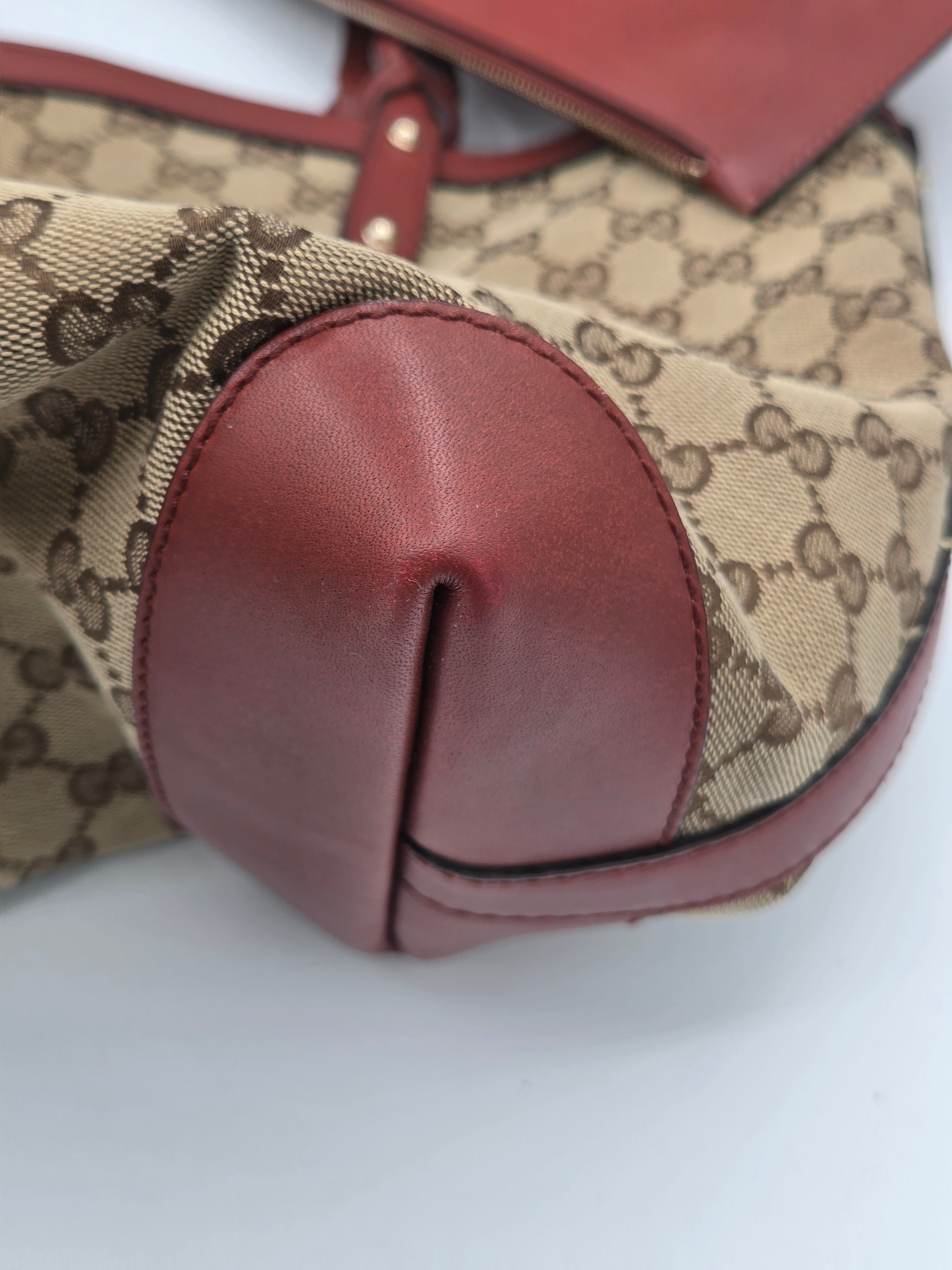 Close-up of a Gucci tote bag featuring the classic brown GG monogram canvas and rich burgundy leather trim, with a gold-tone metal rivet visible on the corner.