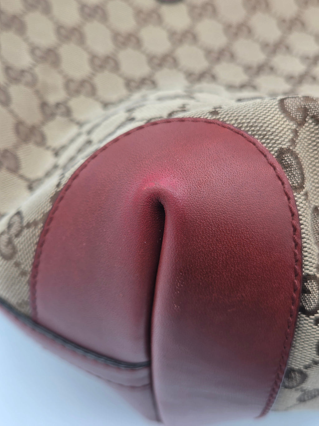Close-up of a Gucci monogram canvas bag with a prominent dark red leather trim and a dark brown monogram pattern.
