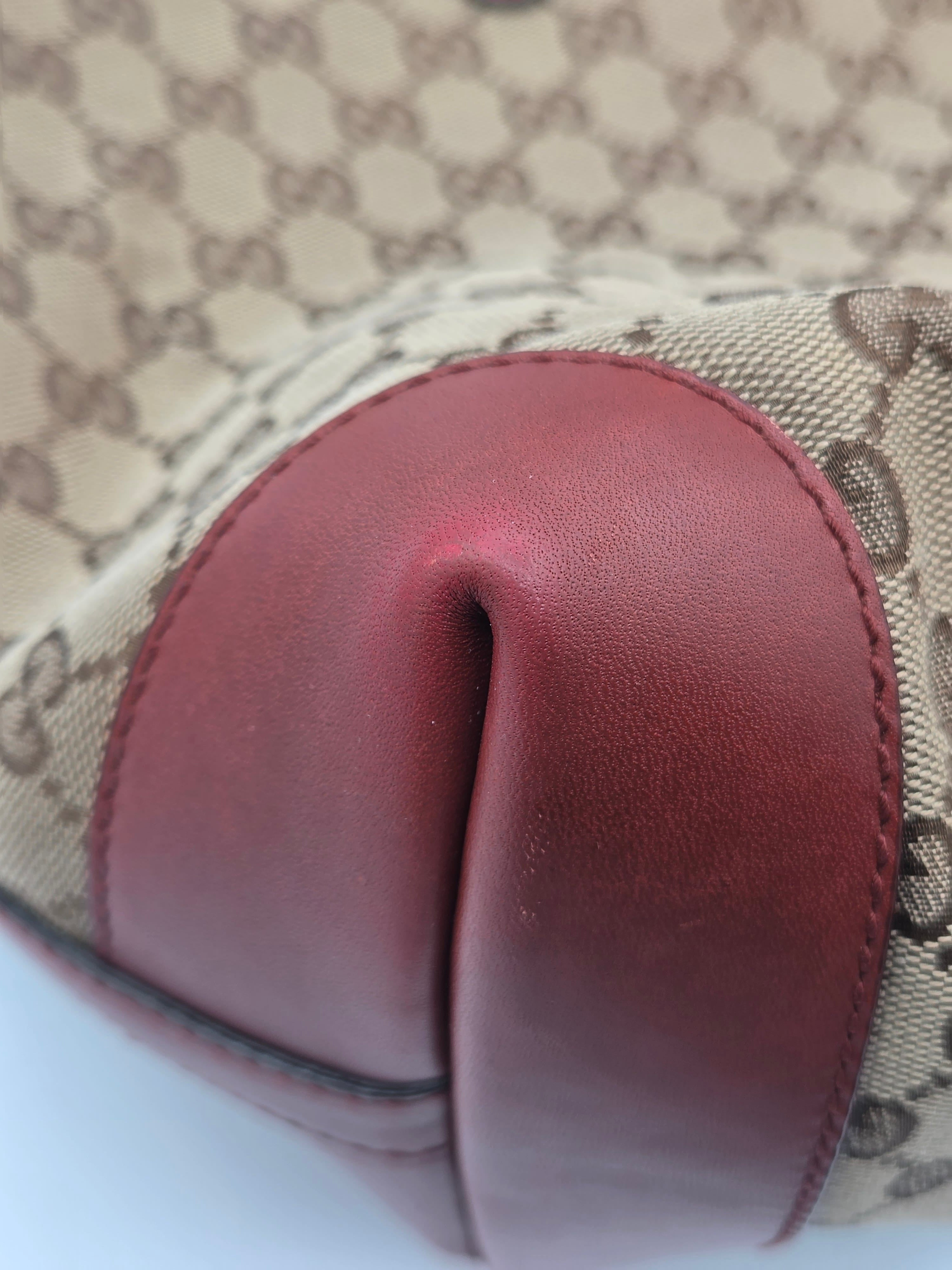 Close-up of a Gucci monogram canvas bag with a prominent dark red leather trim and a dark brown monogram pattern.