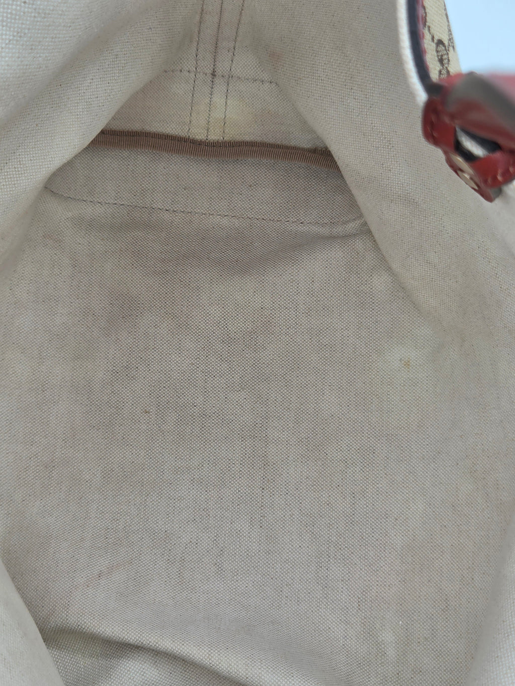Close-up of a beige canvas or linen fabric bag interior with visible stitching and a small red decorative element at the top right.