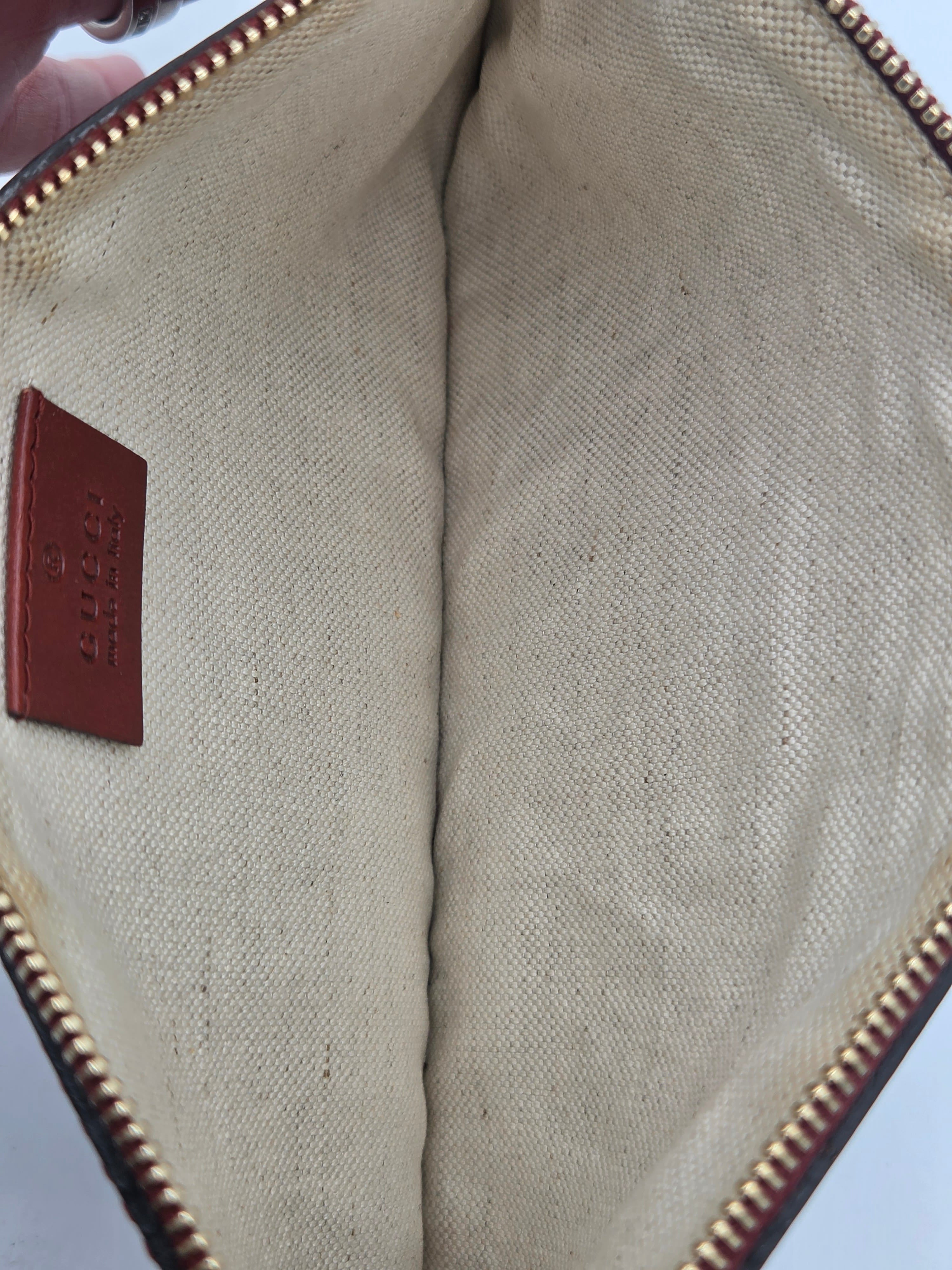 Close-up of the interior of a canvas zippered pouch or clutch, showing a beige woven fabric lining, a brown leather brand patch embossed with 'CLOTHING', and a gold-toned zipper.