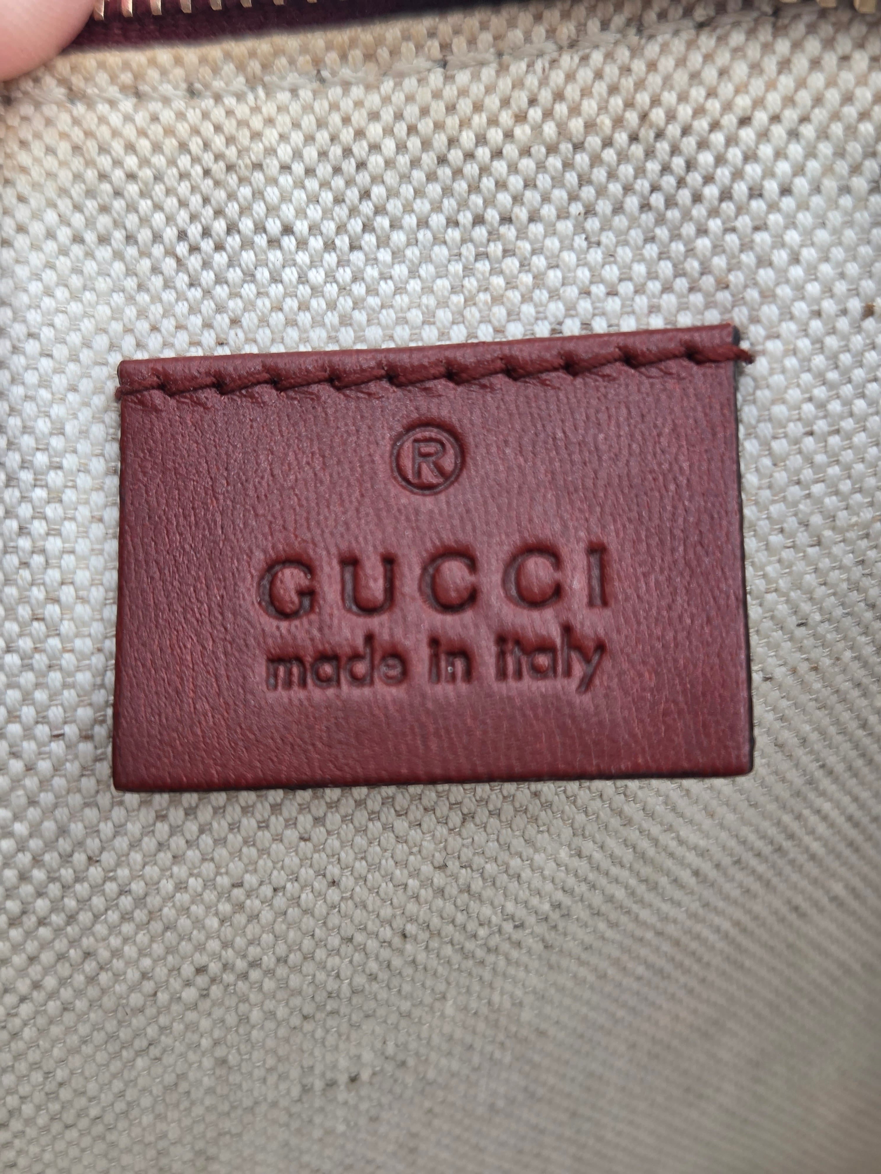 Close-up of a Gucci embossed leather patch on a beige woven canvas background, with 'GUCCI made in italy' visible.