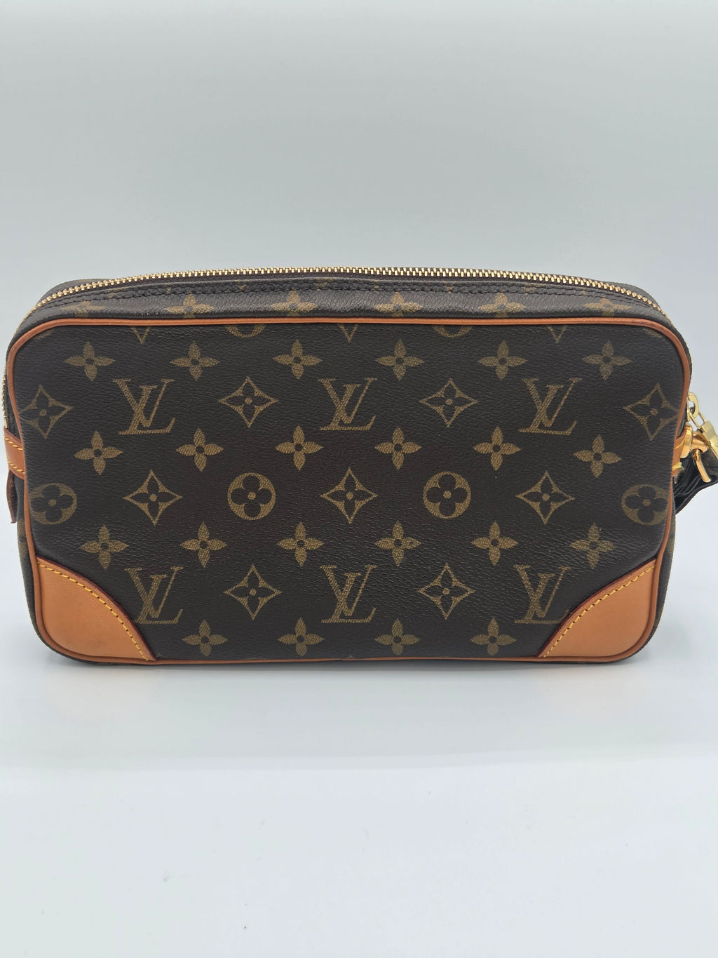 Louis Vuitton monogram canvas pouch with tan leather corner panels and gold-tone zipper, photographed against a light gray studio background.