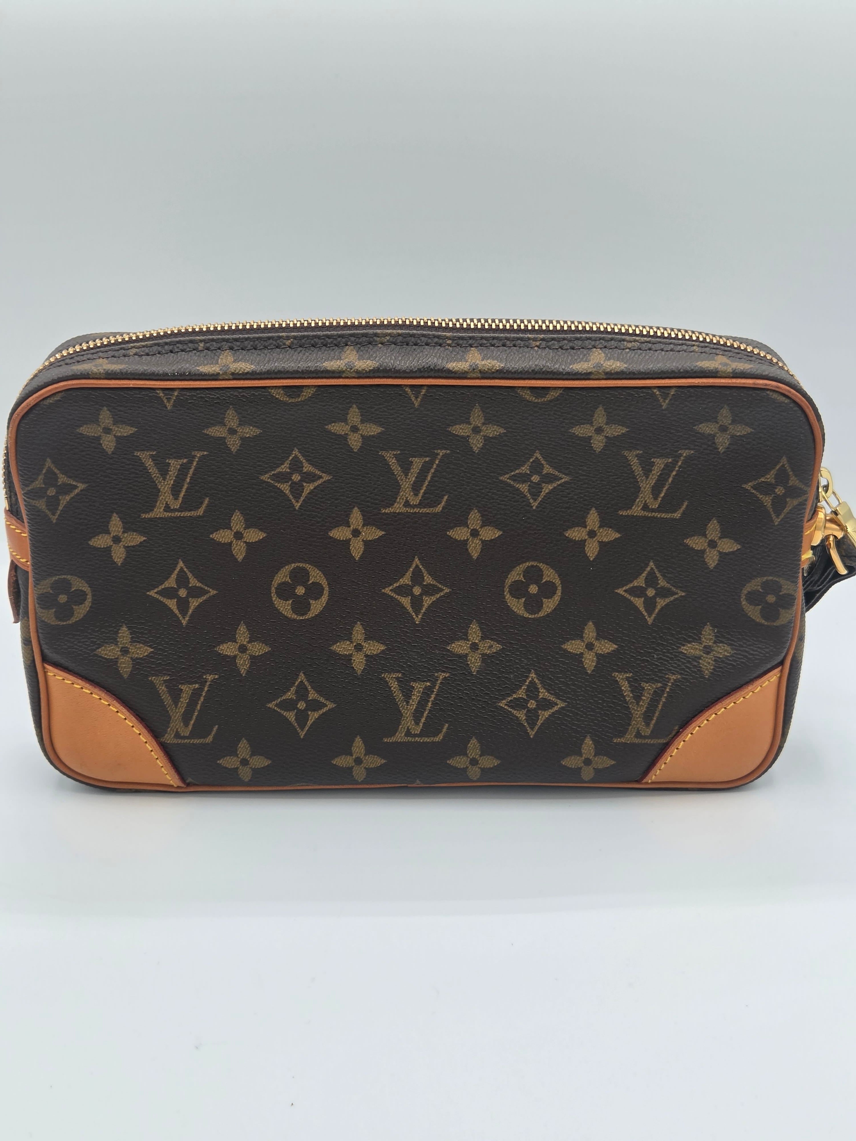 Louis Vuitton monogram canvas pouch with tan leather corner panels and gold-tone zipper, photographed against a light gray studio background.