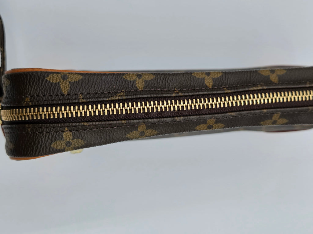 Close-up of a Louis Vuitton monogram canvas zipper pouch showing the classic brown and gold pattern and a gold zipper.