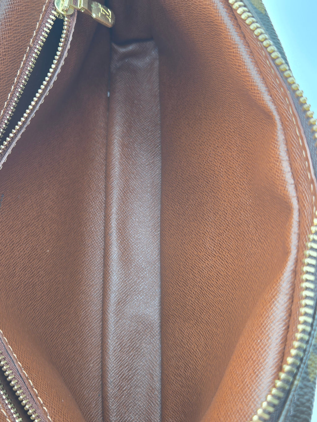 Close-up of the interior of a brown textured leather bag, showing a central seam, gold-tone zipper tracks, and the inner lining.
