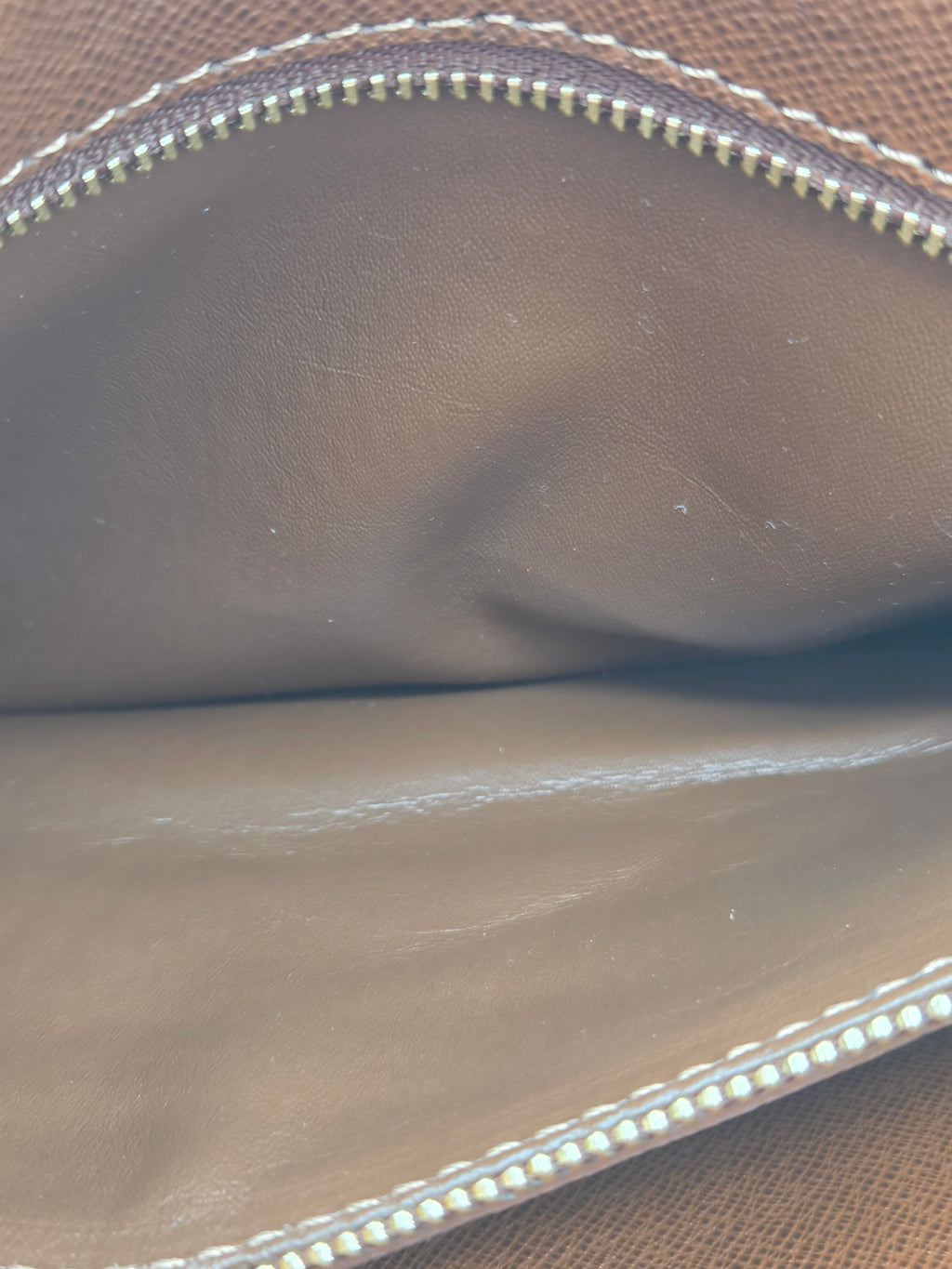 Close-up of the interior lining of a brown leather zippered pouch or wallet, showing the smooth brown interior, white stitching, and a gold-toned zipper.