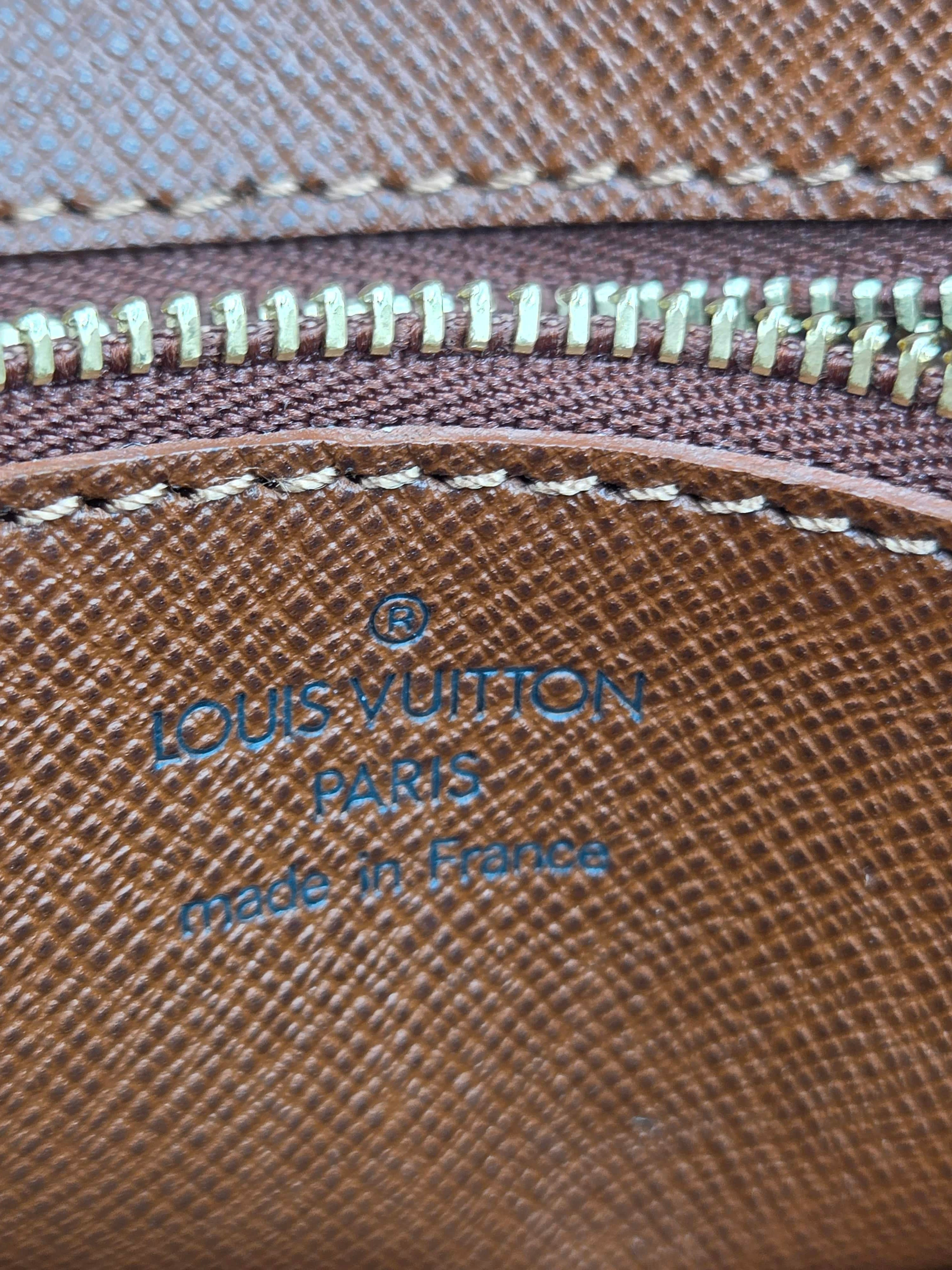 Close-up of a brown Louis Vuitton textured leather zippered pouch with blue embossed branding and white stitching.