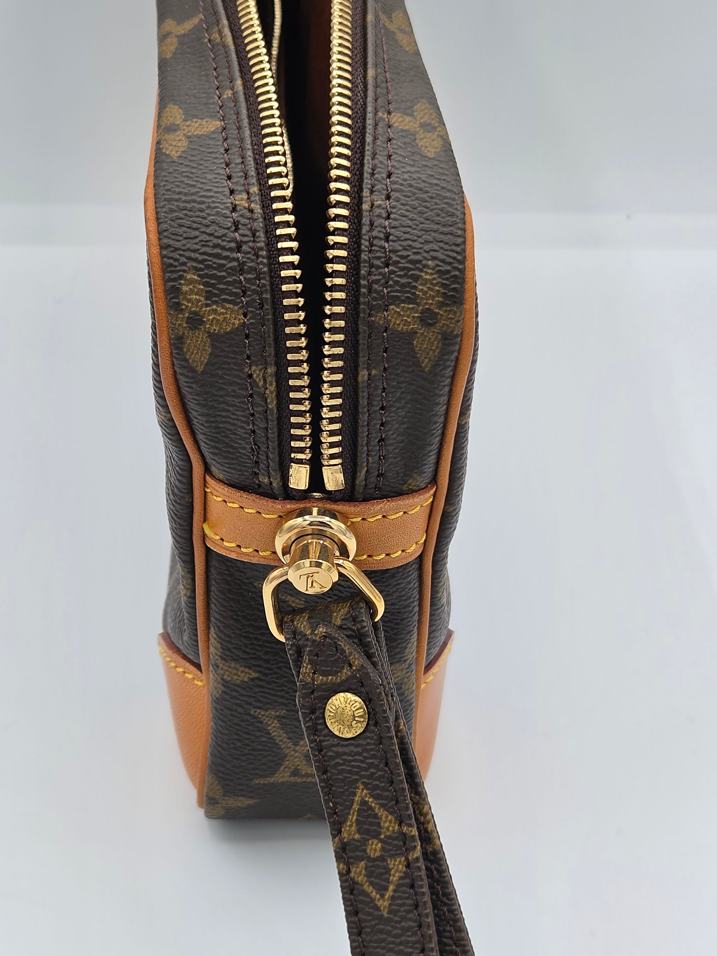 Close-up of a Louis Vuitton monogram canvas bag with tan leather trim and gold-tone hardware, showing the zipper and wristlet strap detail.