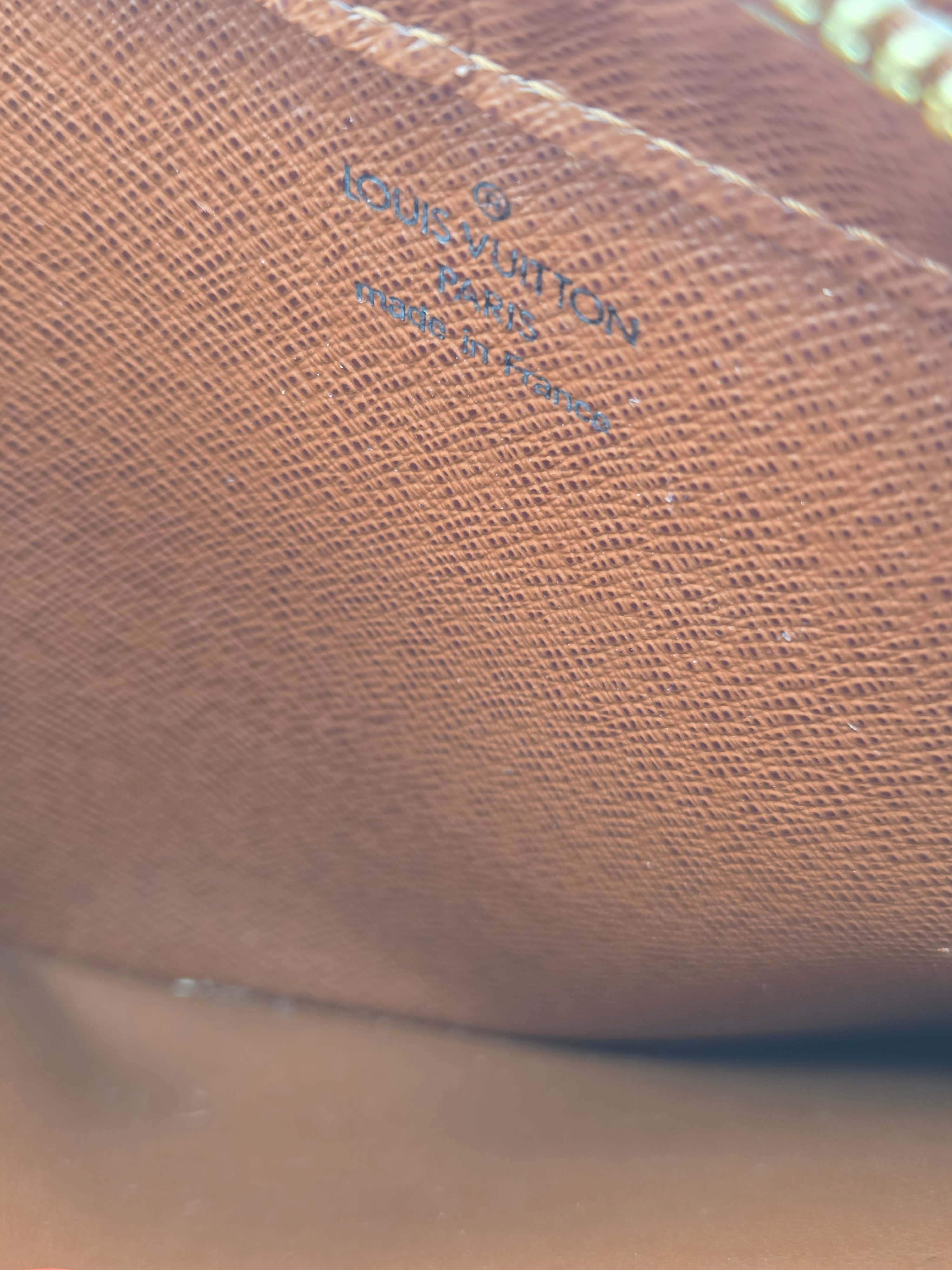 Close-up of a brown textured leather interior with embossed Louis Vuitton branding and a gold zipper pull partially visible at the top edge.