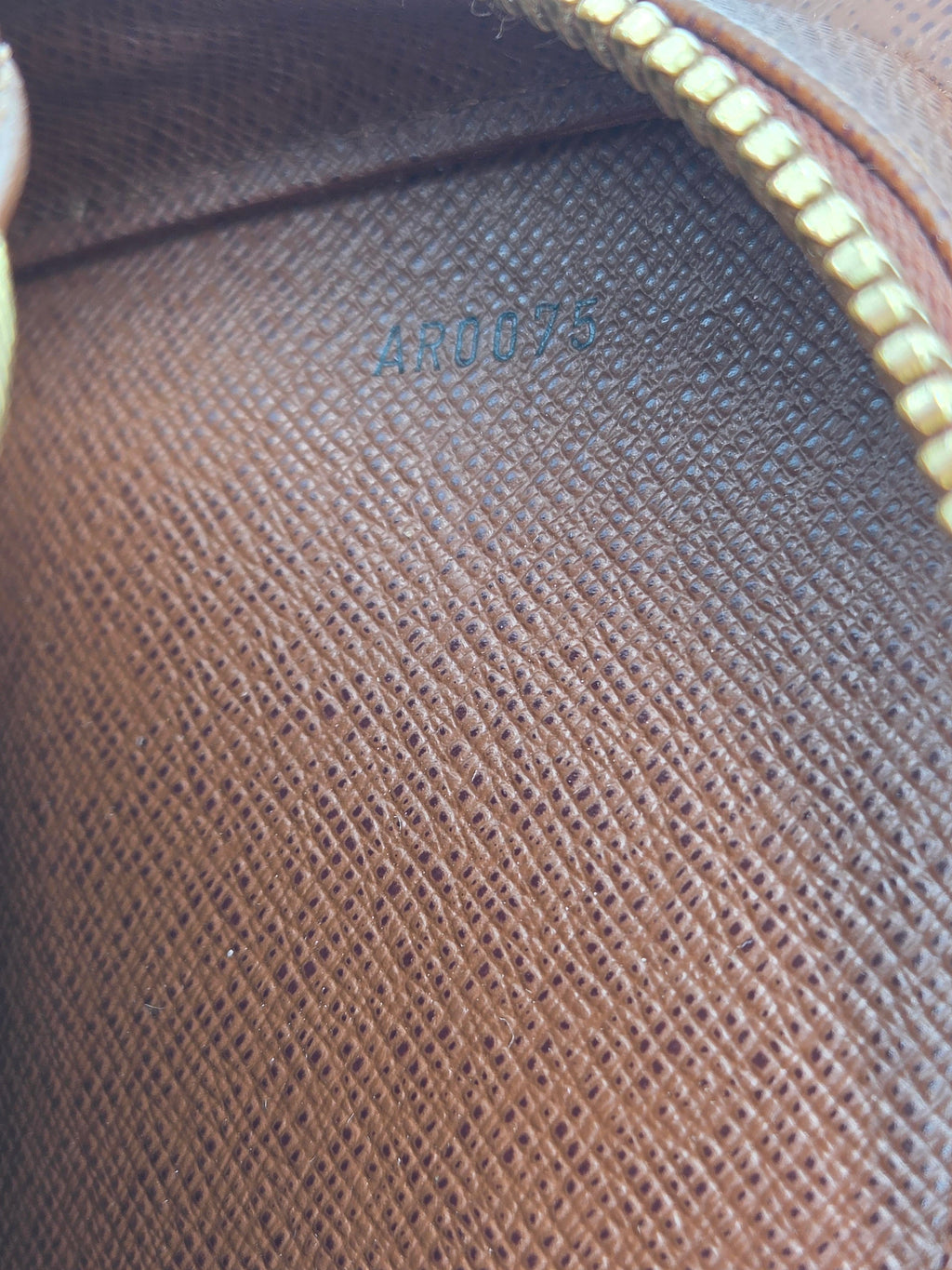 Close-up of a brown textured leather or canvas pouch interior with a gold zipper and embossed blue numbering.