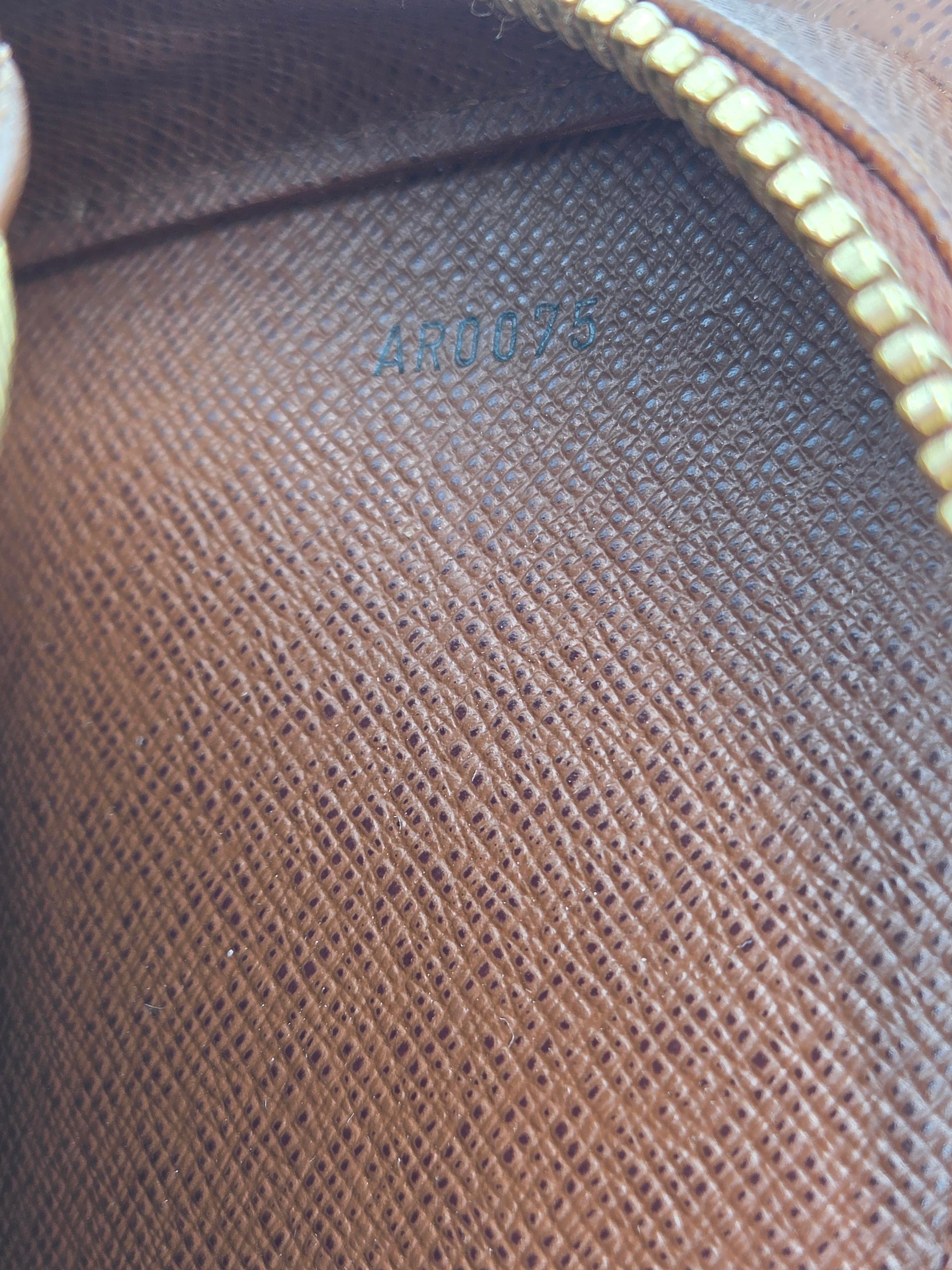 Close-up of a brown textured leather or canvas pouch interior with a gold zipper and embossed blue numbering.