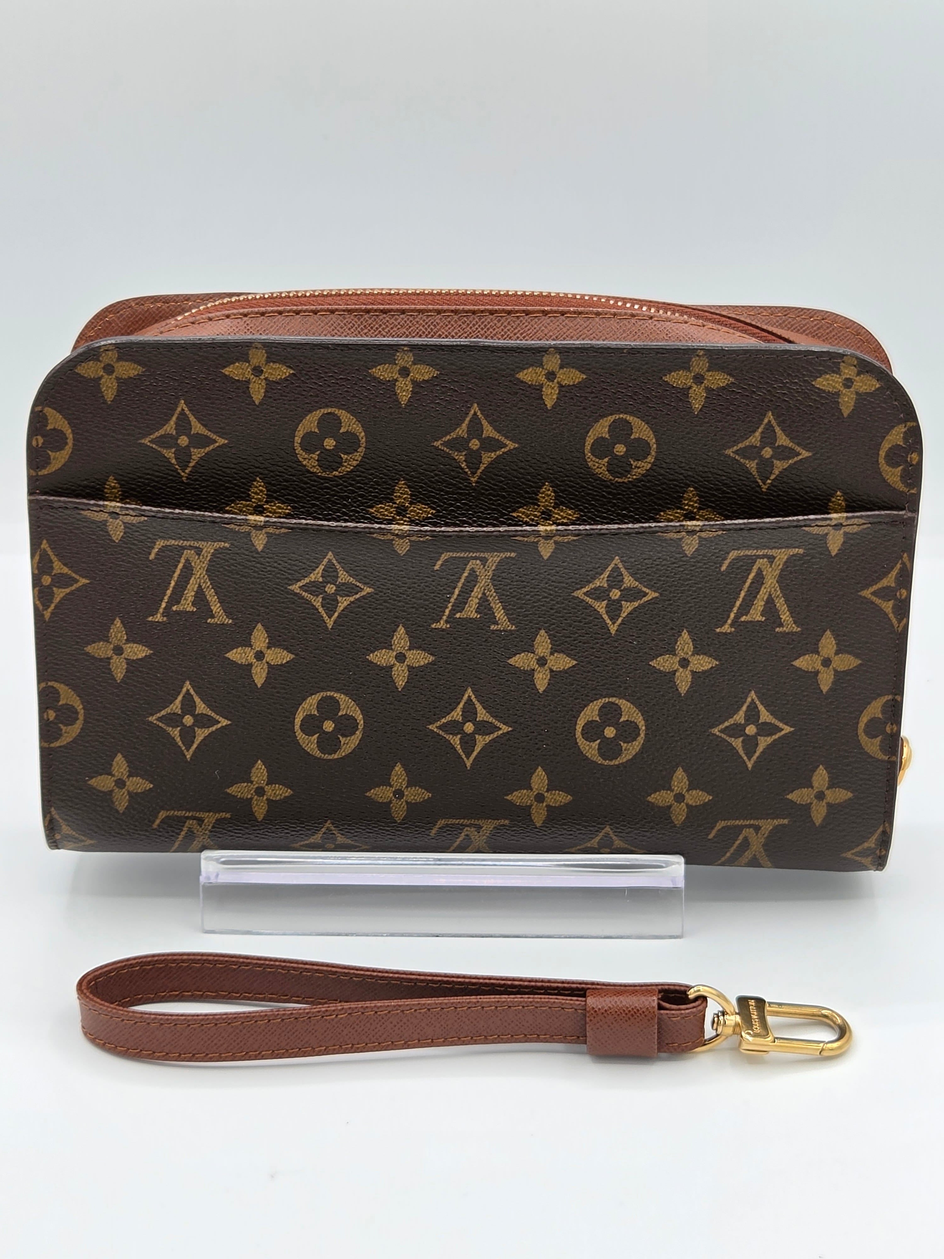 Louis Vuitton monogram canvas pouch with a brown leather wristlet strap and gold-tone hardware, displayed on a white background with a clear stand.