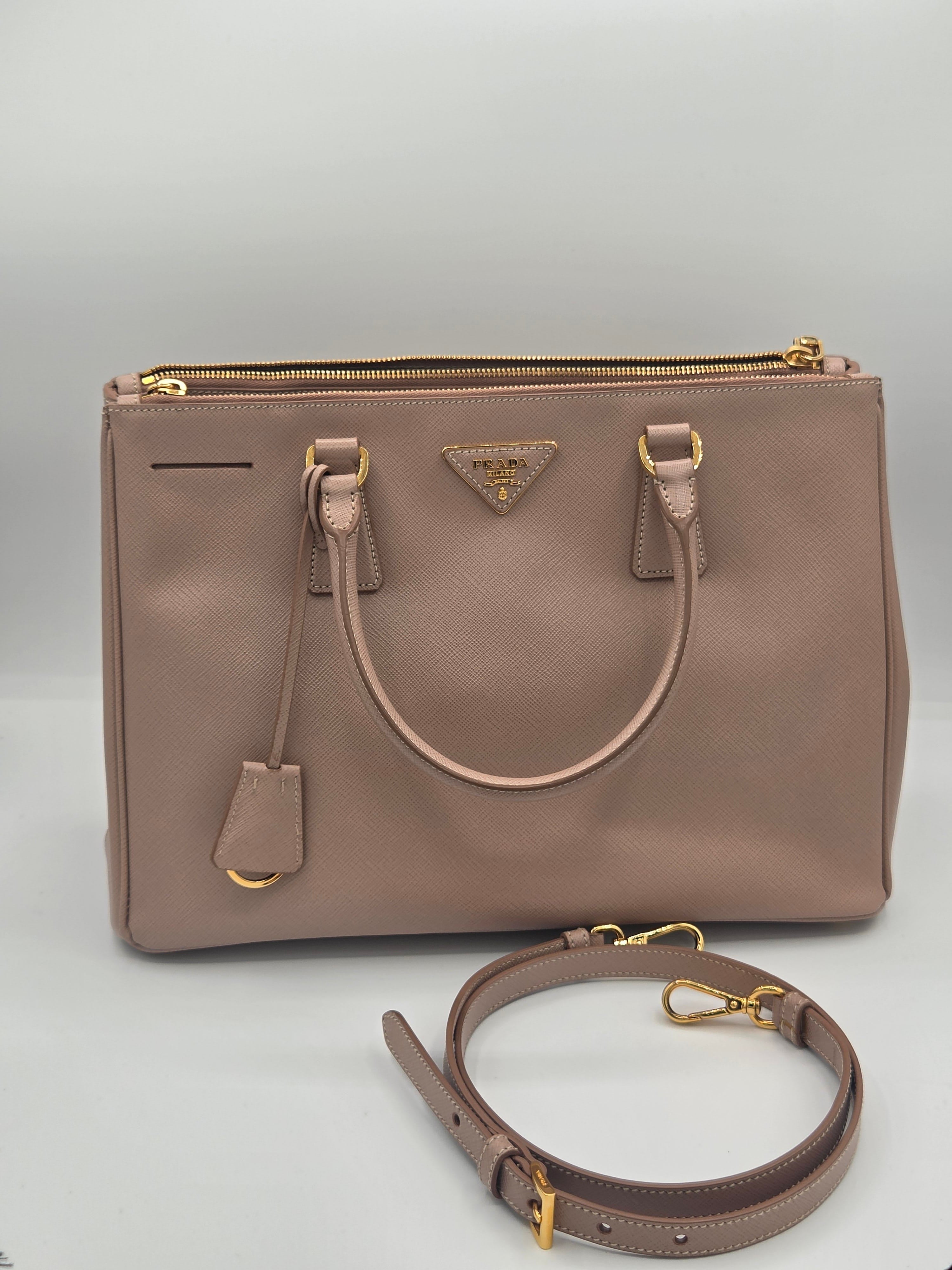 A structured Prada shoulder bag in dusty rose leather with gold-tone hardware, shown with its detachable shoulder strap on a light gray background.
