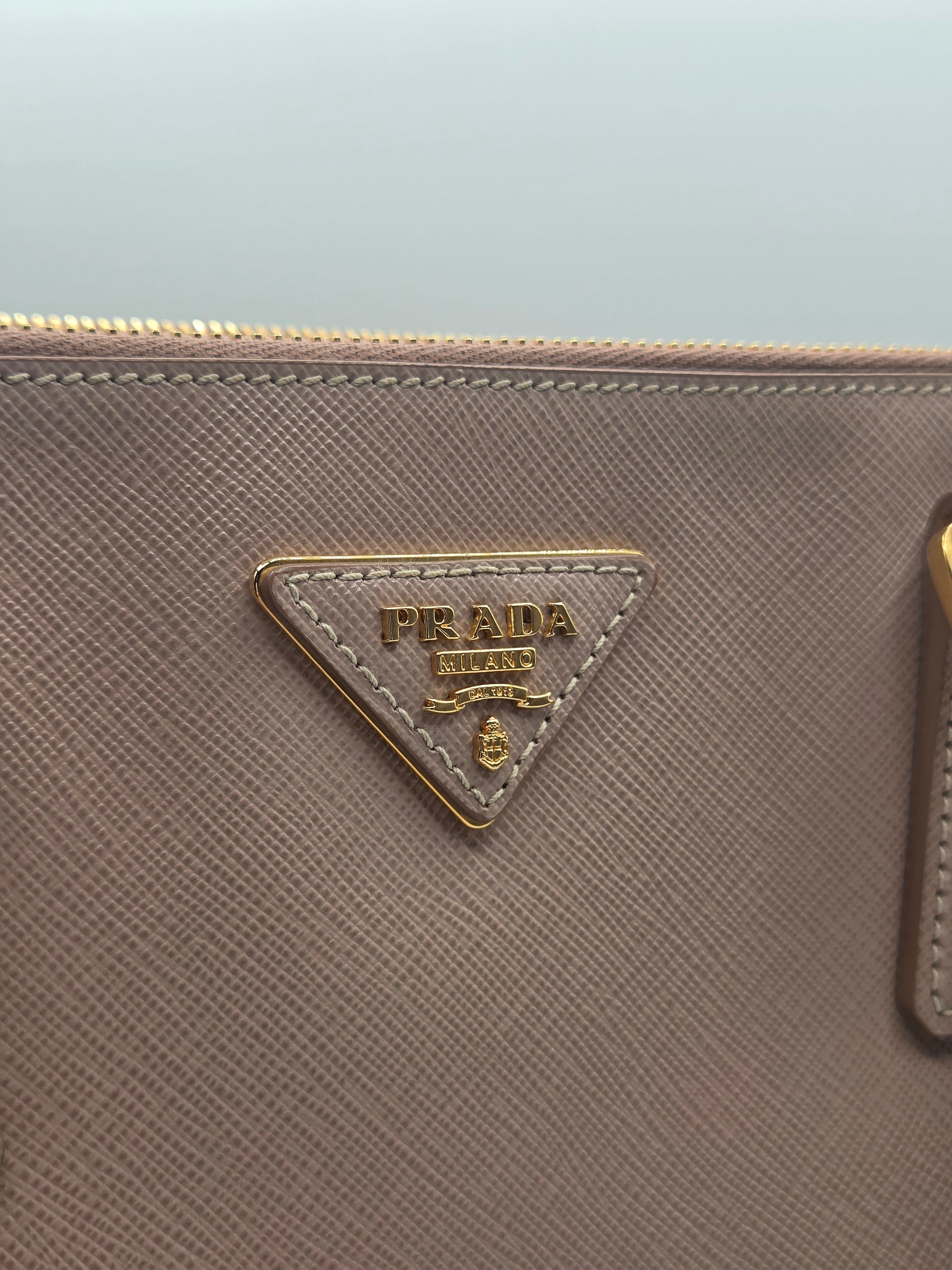 Close-up of a Prada pouch in textured taupe leather with the iconic gold-tone triangular logo plaque on the front.