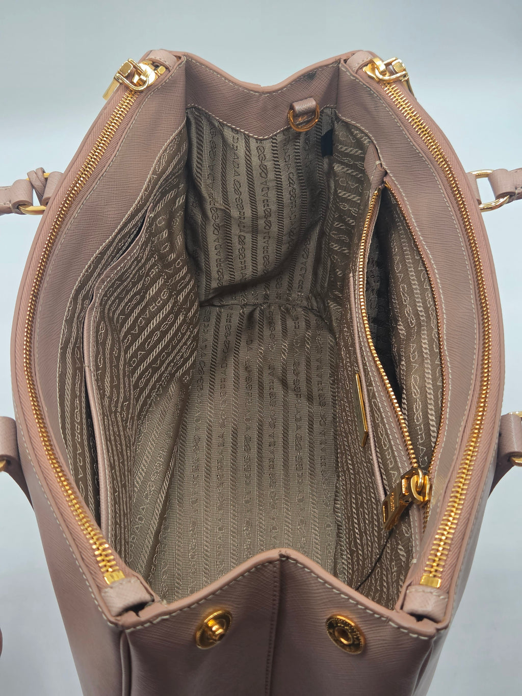 An open taupe leather handbag with gold-tone hardware, showing a striped interior lining and multiple compartments.
