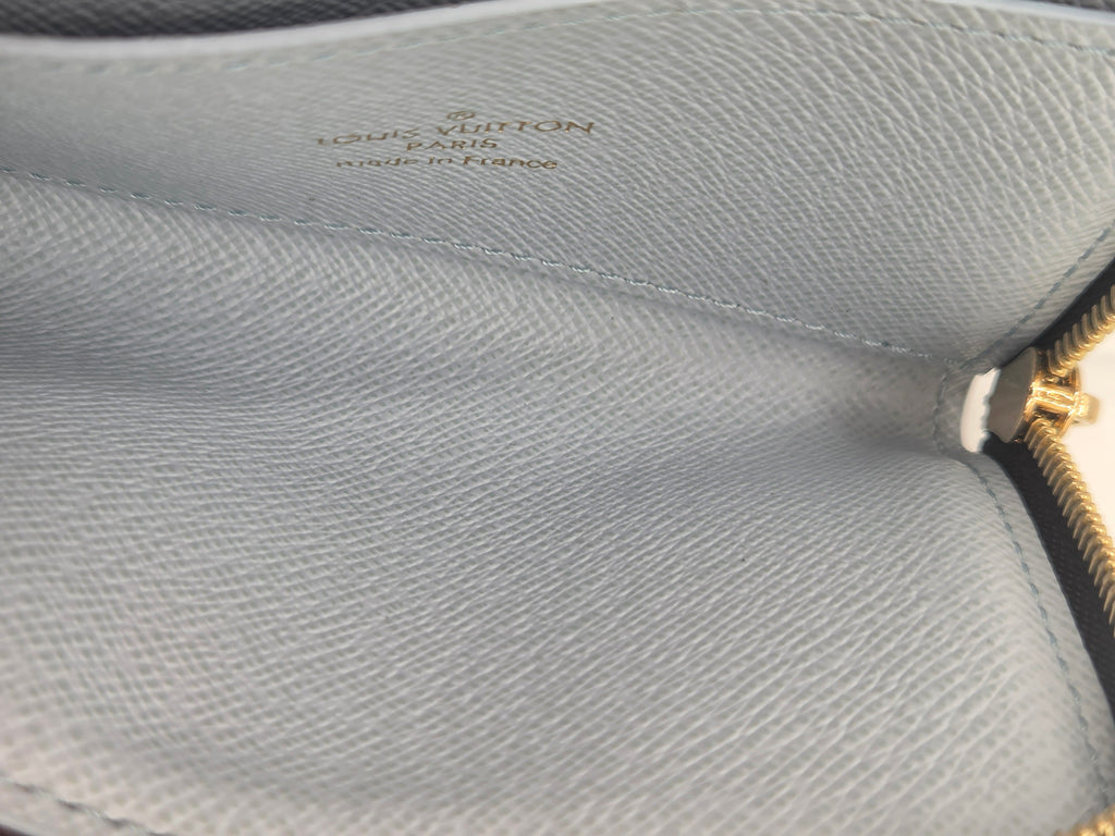Close-up of a Louis Vuitton coin purse interior in light blue textured leather with gold foil branding and a gold zipper pull.