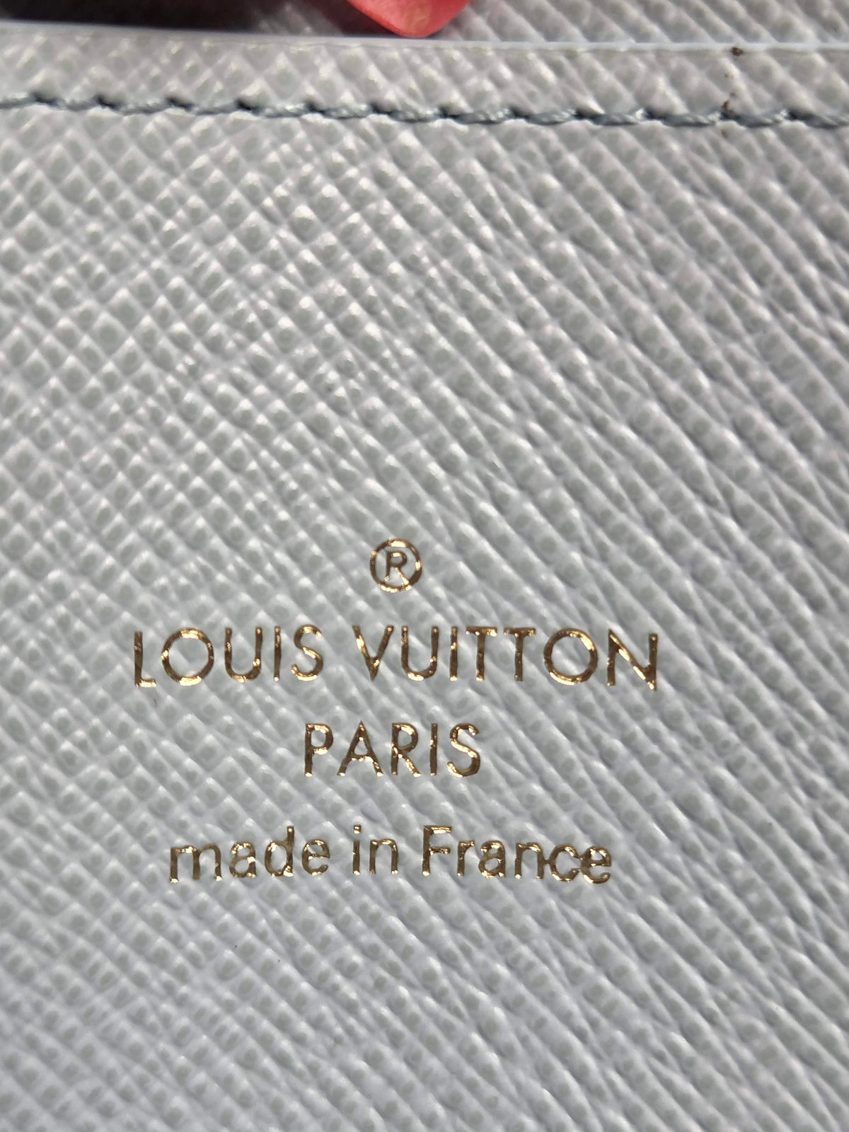 Close-up of a light gray textured leather surface with gold-toned Louis Vuitton Paris branding and 'made in France' text.