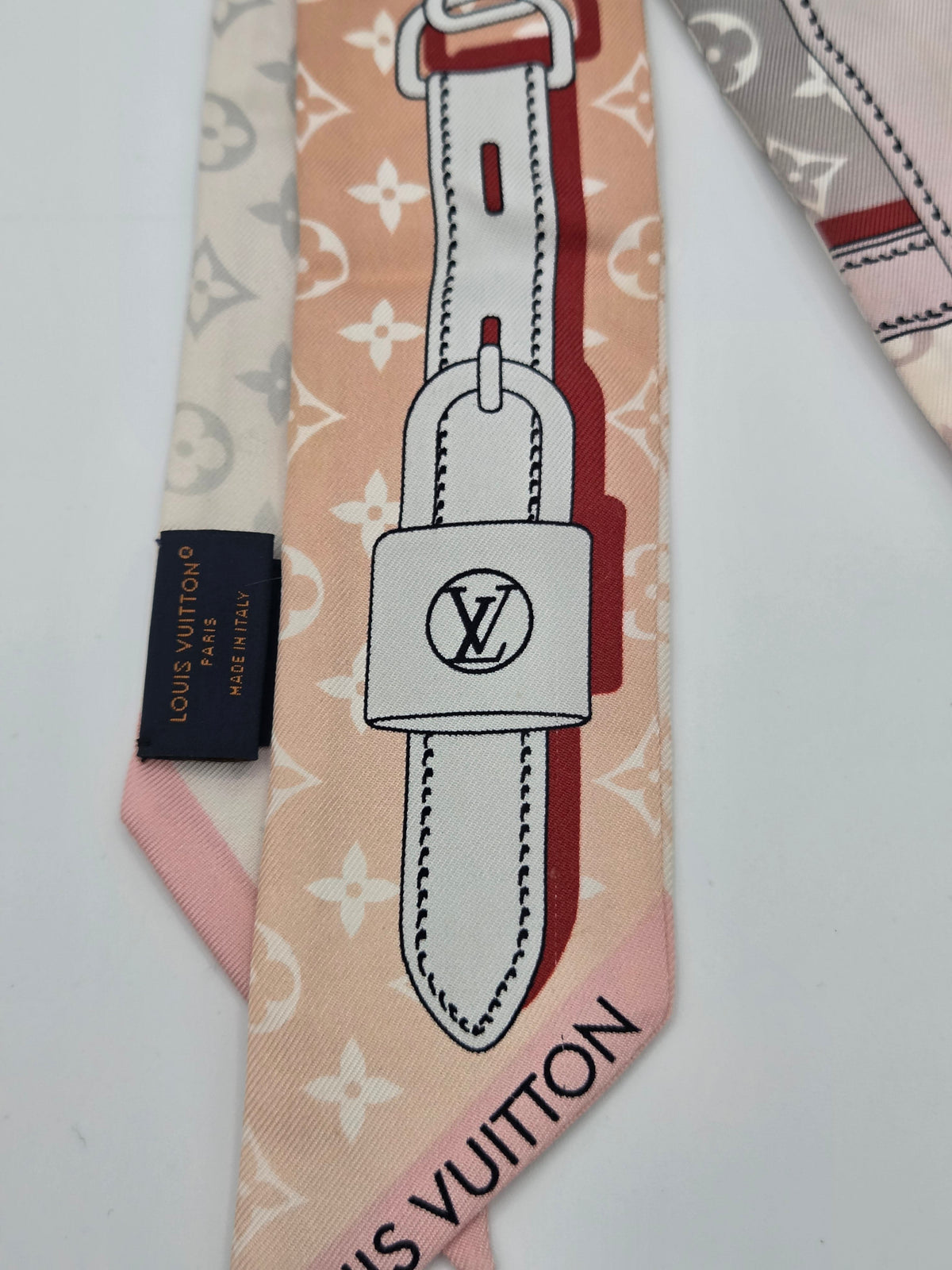 A Louis Vuitton silk scarf featuring a pastel pink and beige monogram pattern, a large white padlock graphic with the LV logo, and a black brand tag.