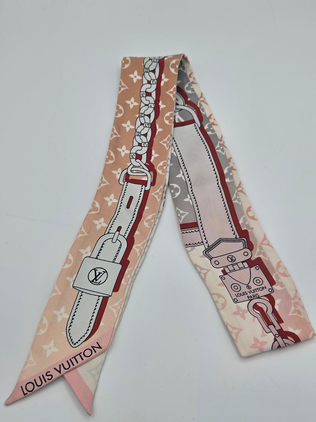 A Louis Vuitton silk scarf featuring a monogram pattern and a graphic print of a leather strap with padlock and key details, in shades of pink, beige, and white.