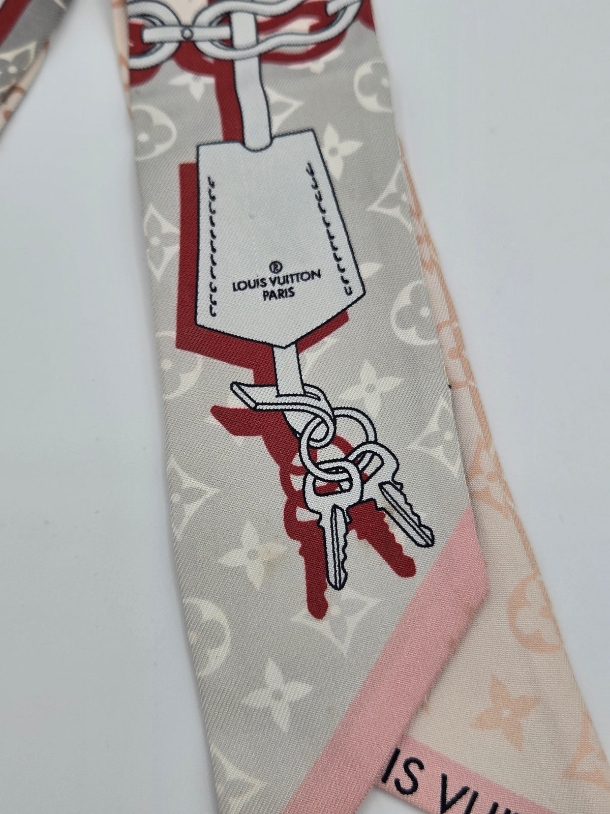 A Louis Vuitton monogram scarf featuring a graphic print of keys and a luggage tag with 'LOUIS VUITTON PARIS' text, shown on a white background.