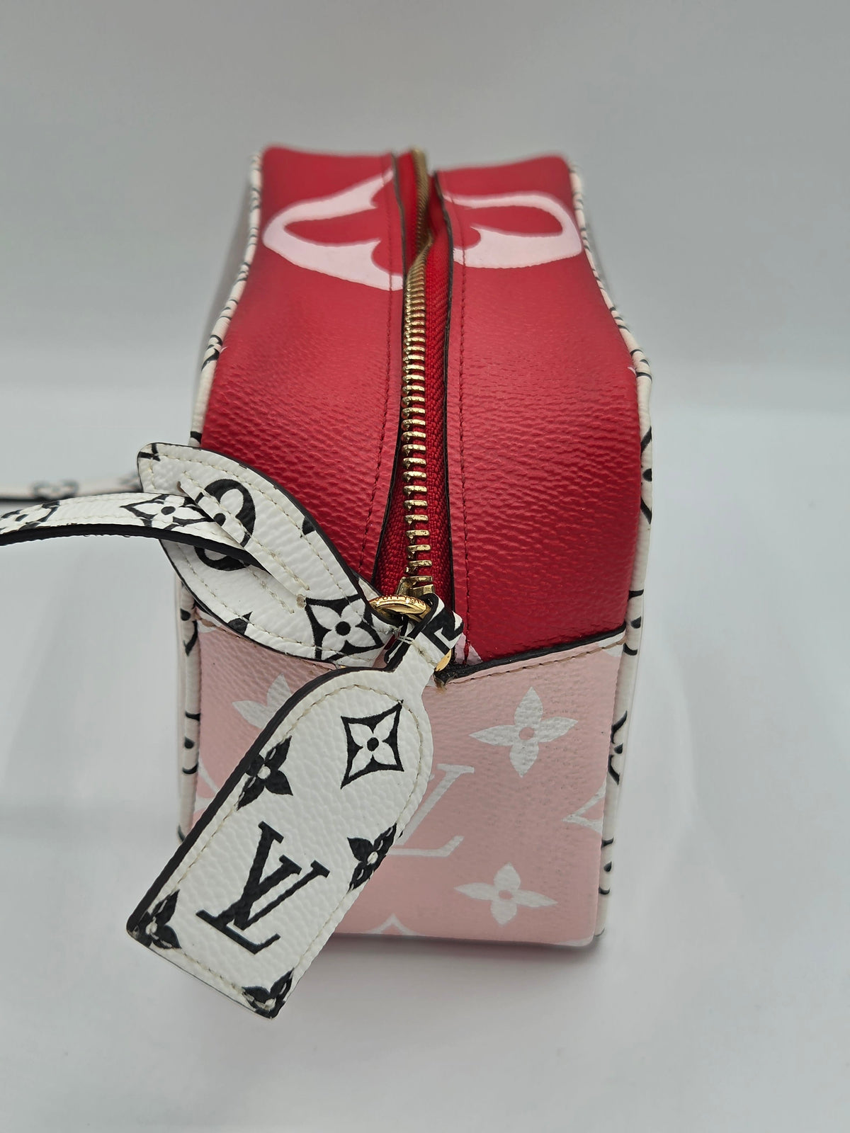 A Louis Vuitton cosmetic pouch featuring a red textured leather top, a light pink monogram canvas base, and a white monogram ribbon tie, shown on a neutral light gray background.