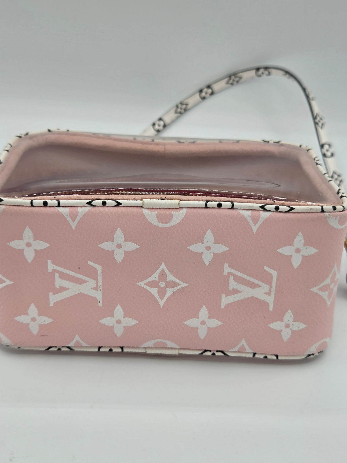 A pink Louis Vuitton monogram canvas handbag with a white monogram pattern, featuring a clear zippered top and a matching patterned strap, set against a plain light gray background.