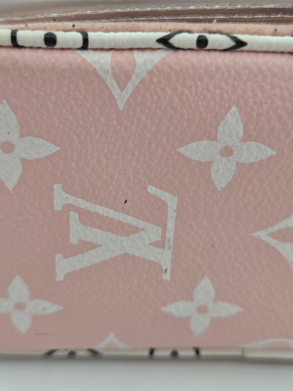 Close-up of a pink Louis Vuitton monogram canvas item, showing the white LV logo and floral motifs on textured leather.