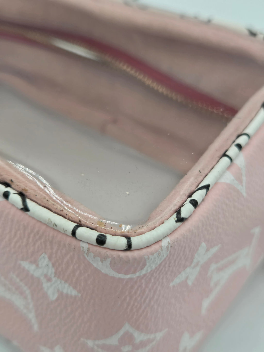 Close-up of a pink Louis Vuitton monogram pouch or case with a clear plastic insert inside, showing the white monogram pattern and black-and-white striped trim.