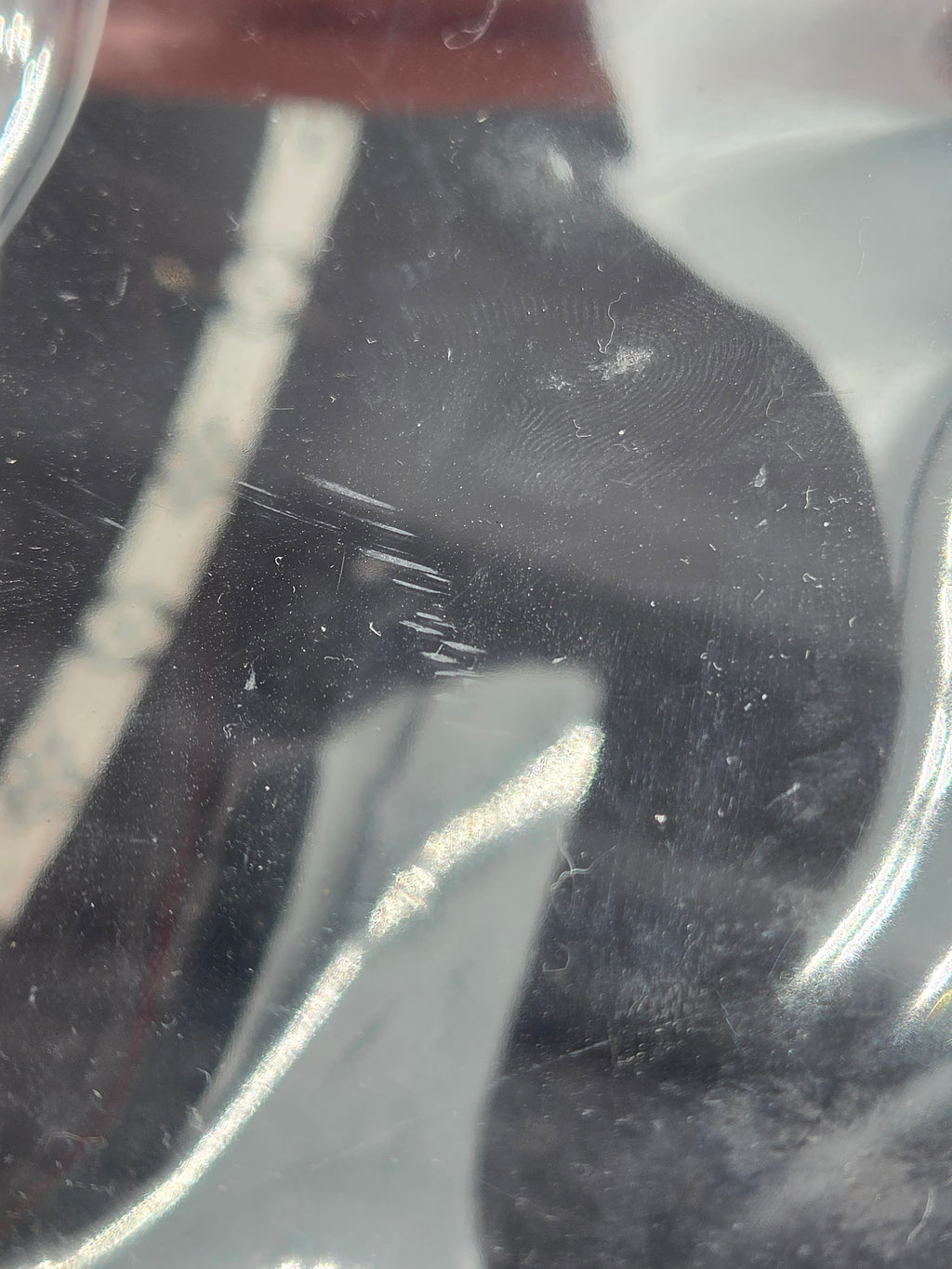 Close-up of a clear plastic surface with visible dust, scratches, and reflections over a dark background.