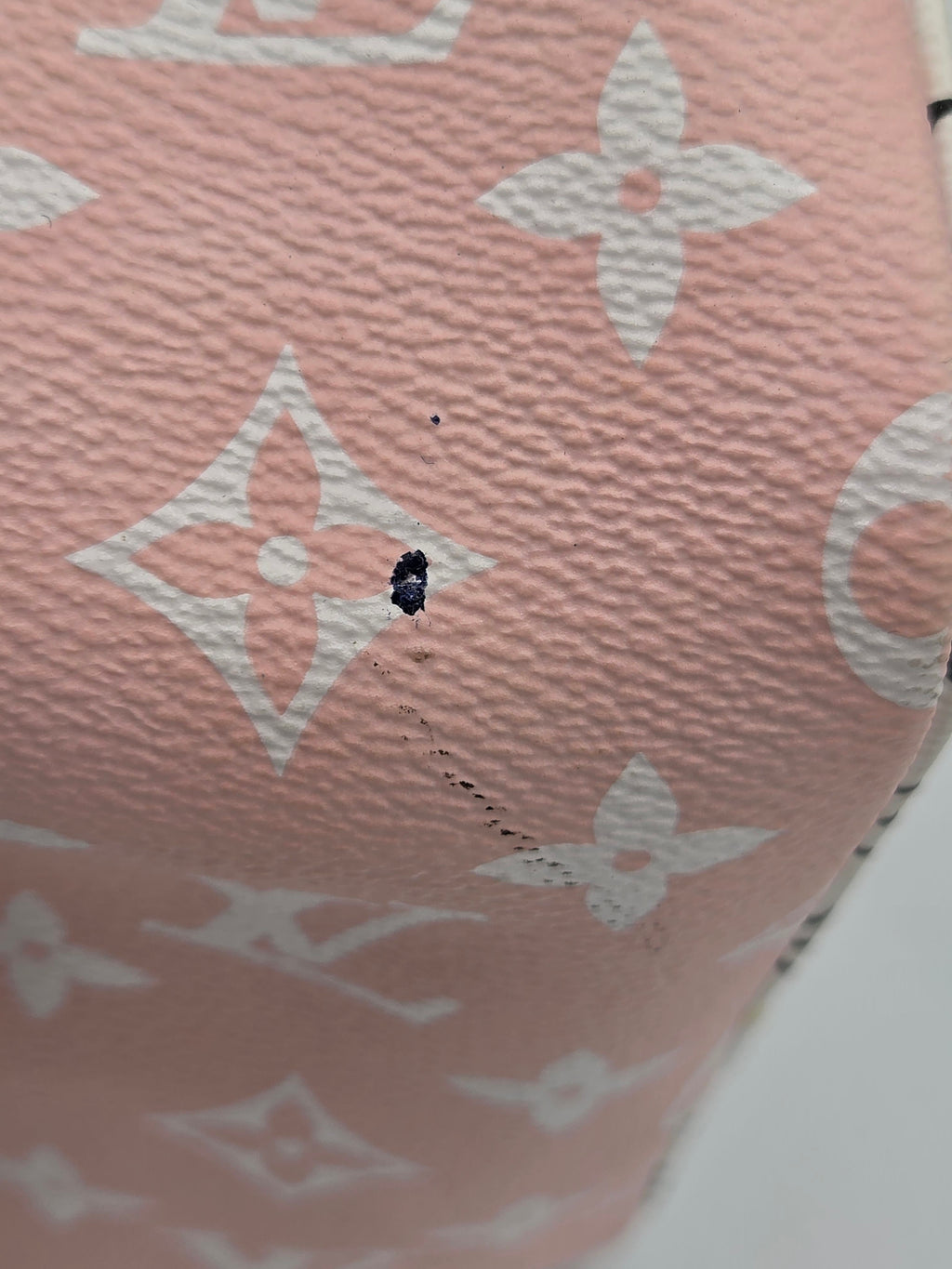 Close-up of a pink Louis Vuitton monogram canvas item with white floral and LV logos, showing a small dark stain or hole on the surface.