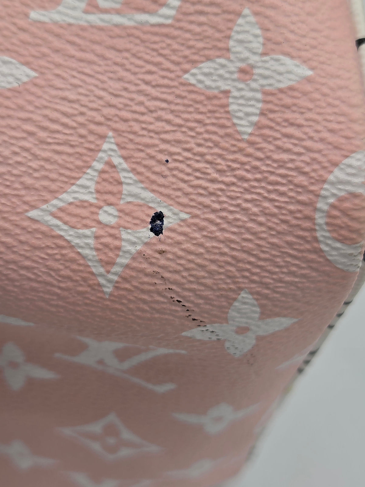 Close-up of a pink Louis Vuitton monogram canvas item with white floral and LV logos, showing a small dark stain or hole on the surface.