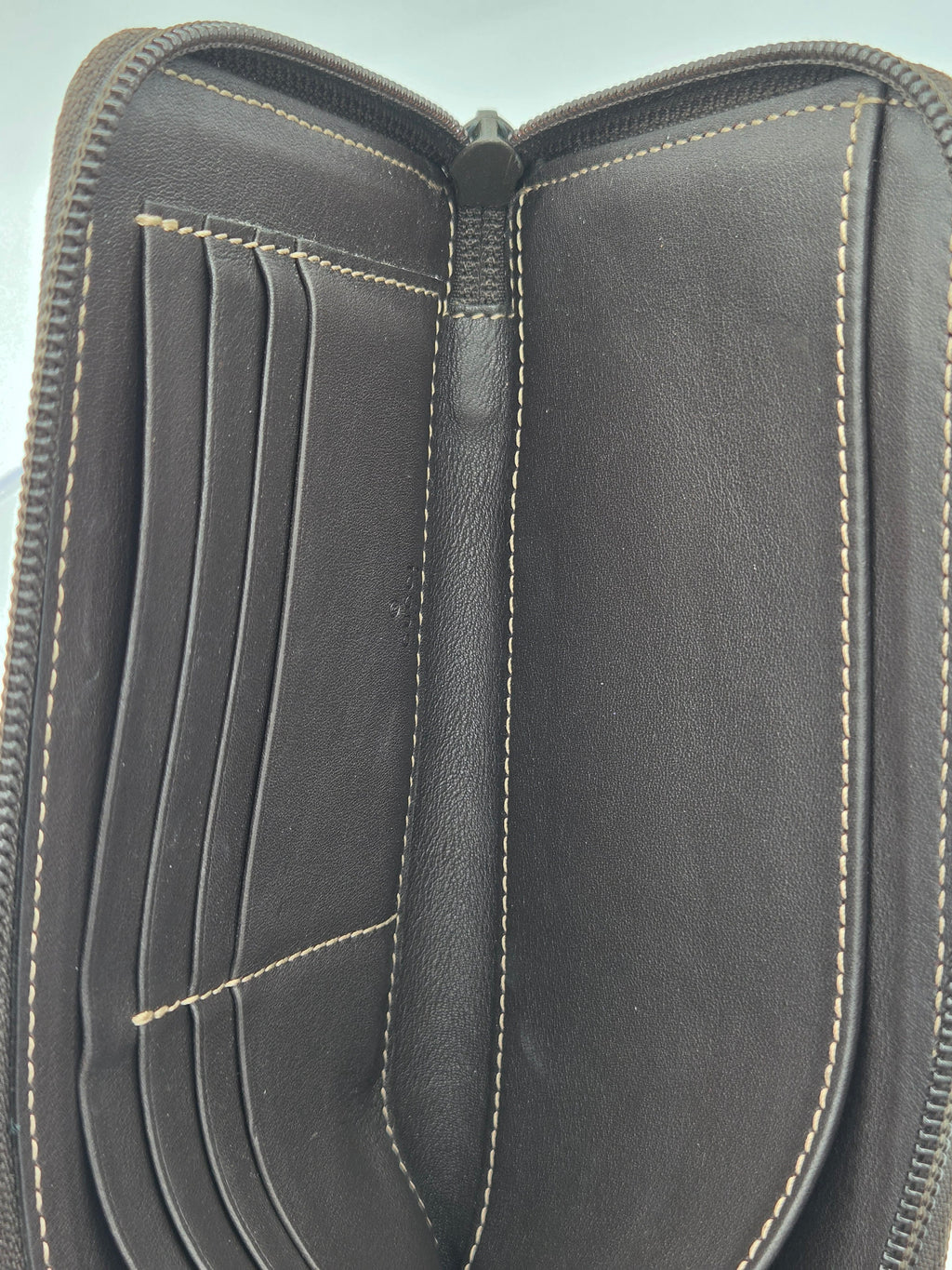 Close-up of an open black leather zip-around wallet showing the interior card slots, center divider, and contrast light tan stitching.